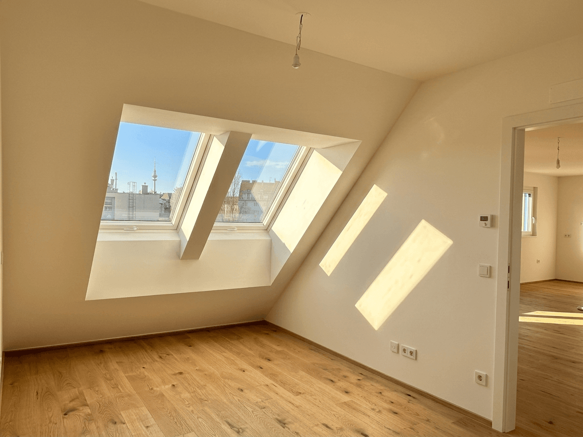 Helles Dachzimmer mit Holzboden und großen Dachfenstern, ideal als Schlafzimmer.