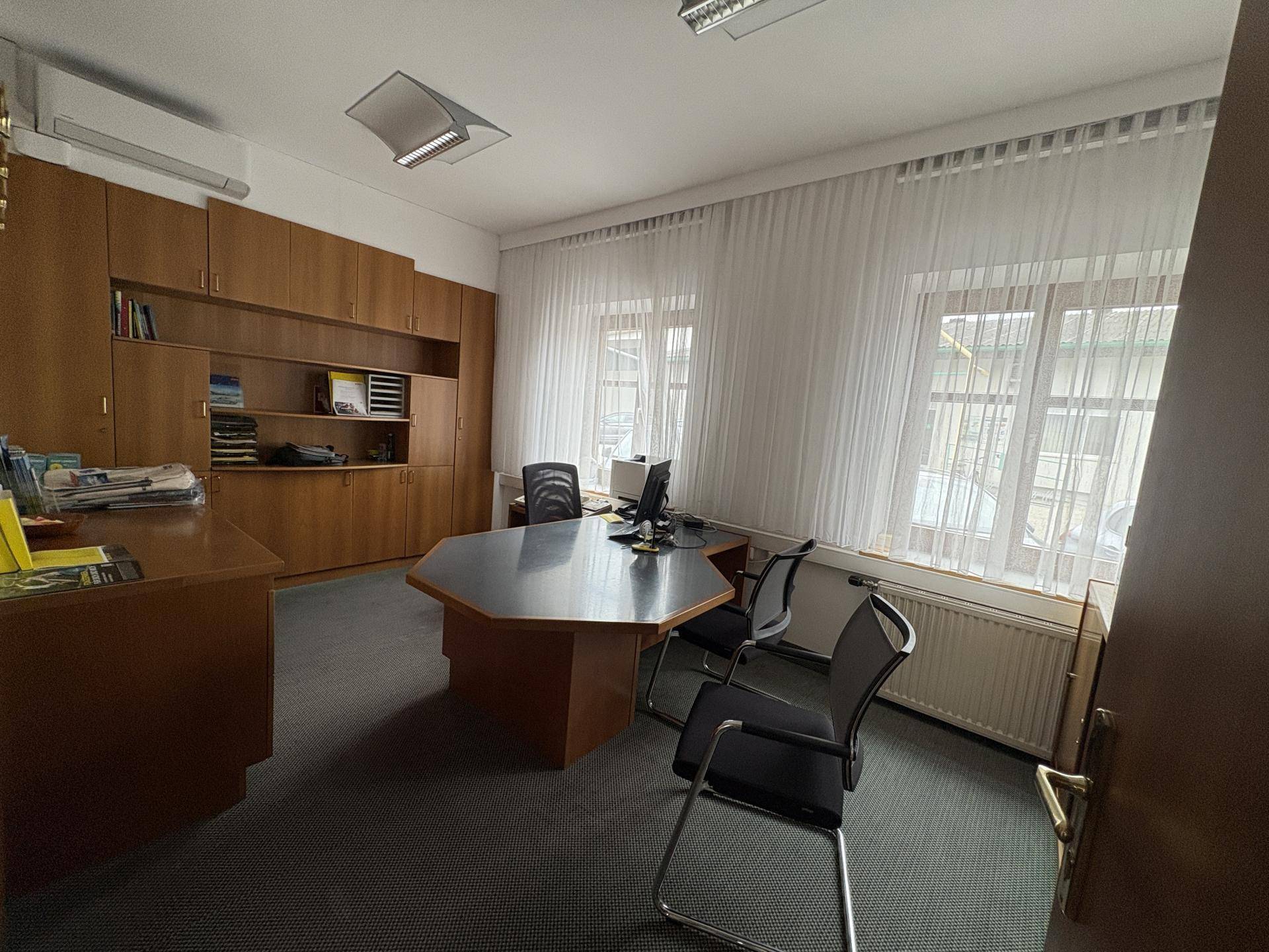 Geräumiges Büro mit Teppichboden, Einbauschränken und einem großen Schreibtisch mit Blick nach draußen.