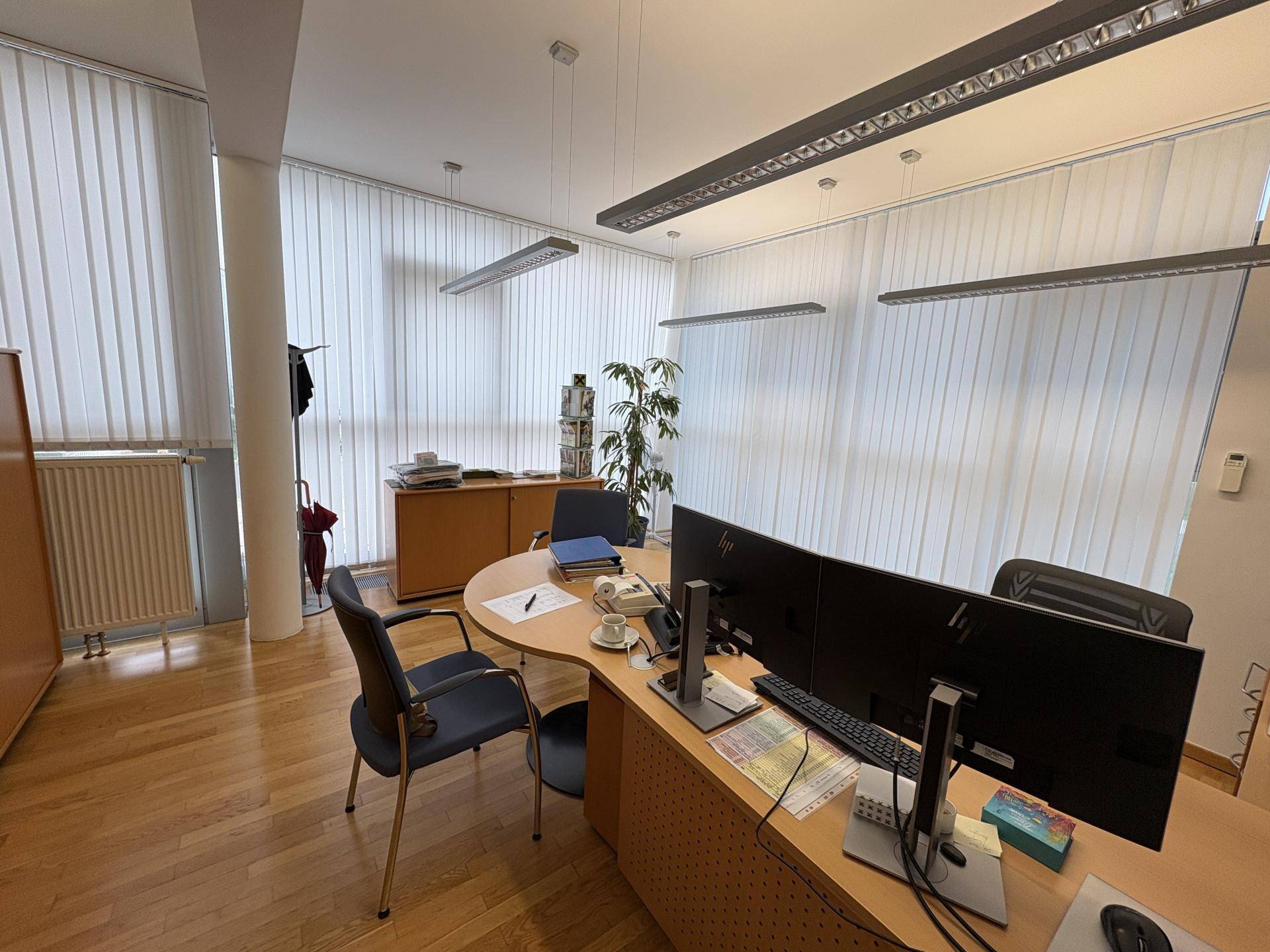 Modernes Büro mit Holzparkettboden, großem Schreibtisch und vertikalen Jalousien an den Fenstern.