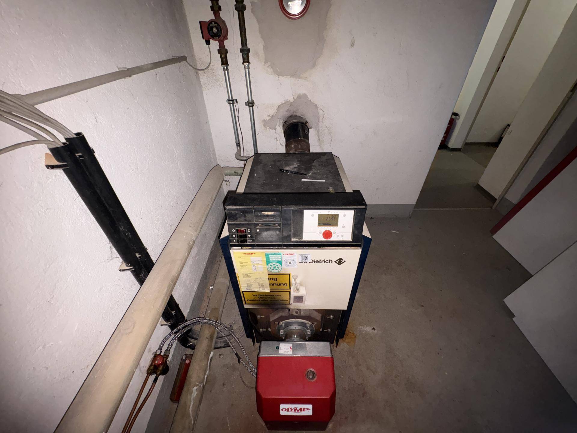 Heizungsraum im Keller mit einem großen Heizkessel und sichtbaren Rohren an der Wand.