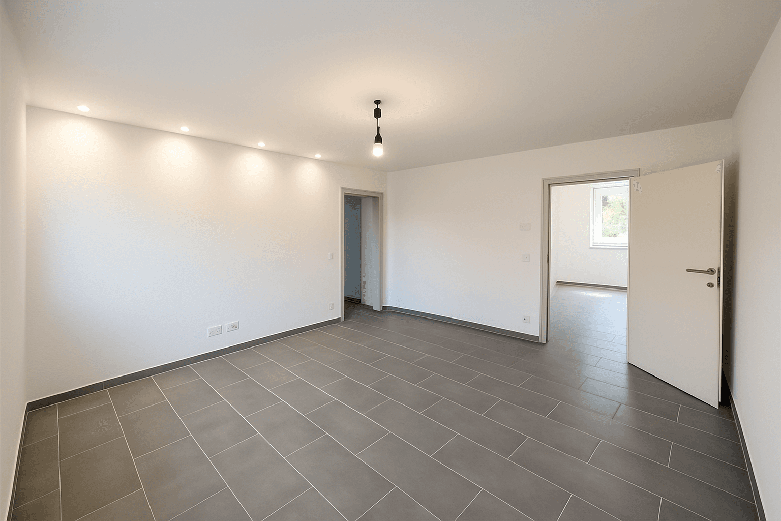 Heller, leerer Raum mit modernen grauen Fliesen und Einbaustrahlern an der Decke.
