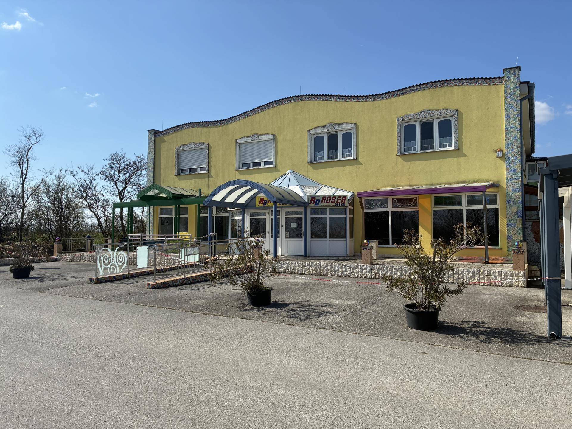 Gebäude mit gelber Fassade, geschwungenem Dach und mehreren Eingängen unter einem blauen Himmel.