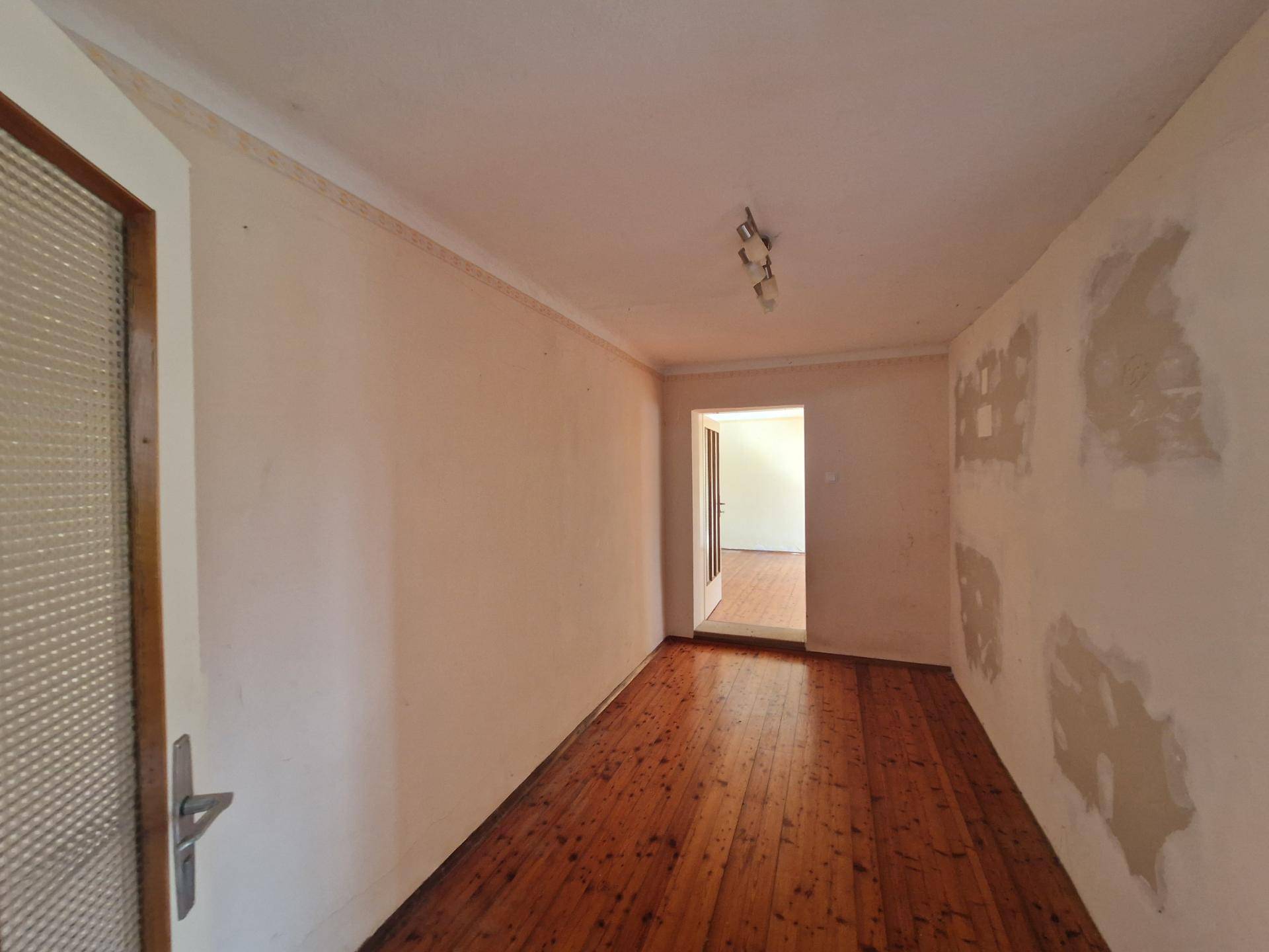 Langer Flur mit Holzdielenboden und sichtbaren Spuren früherer Renovierungsarbeiten.