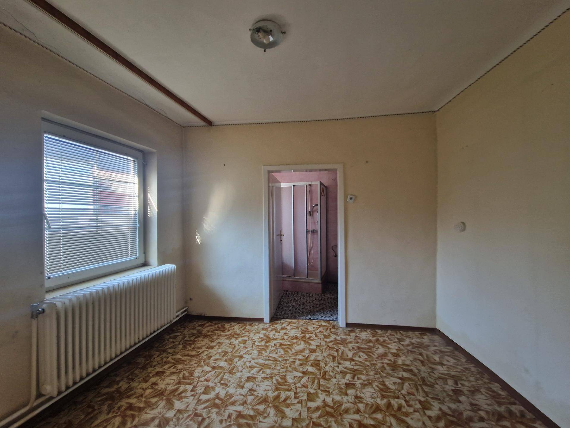 Kleines Zimmer mit gemustertem Bodenbelag und einem Fenster, das Tageslicht hereinlässt.