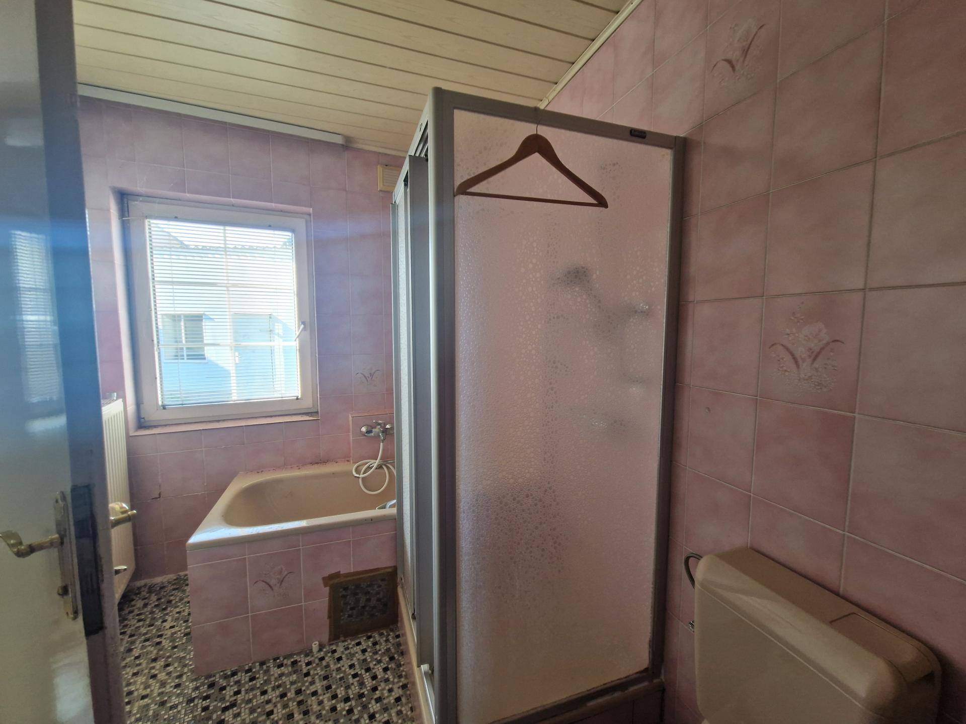 Badezimmer mit rosa Fliesen, Badewanne und Duschkabine, das Renovierung benötigt.