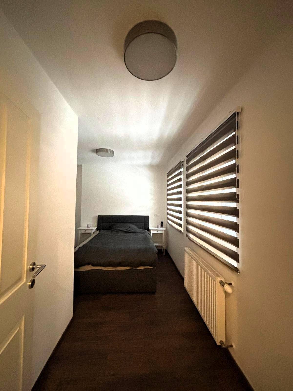 Langes Schlafzimmer mit Doppelbett und Fensterfront, die viel Tageslicht hereinlässt.