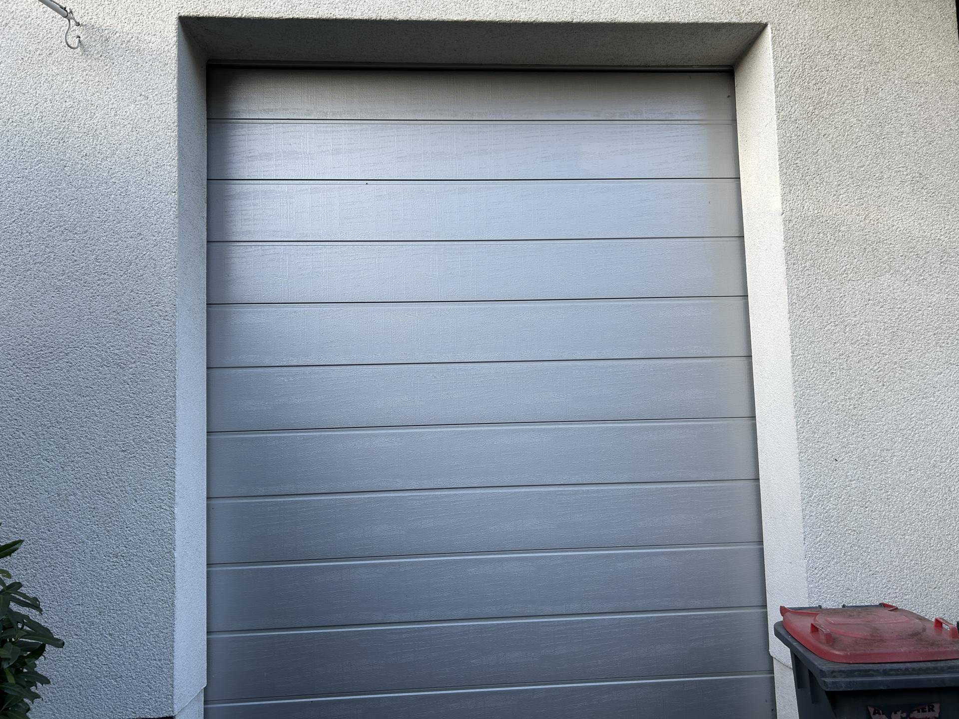 Modernes Garagentor in Grau, bündig in die helle Hauswand integriert.