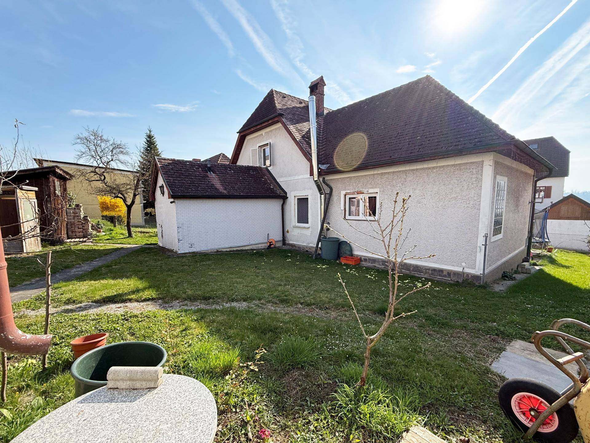 Hinterhof des Hauses mit Rasenfläche, Bäumen und einem kleinen Anbau bei Sonnenschein.