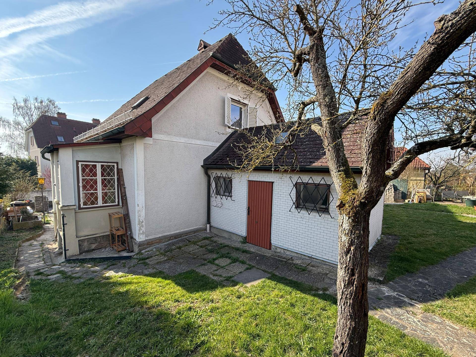 Seitenansicht des Hauses mit Anbau, gepflastertem Bereich und Garten mit Baum.