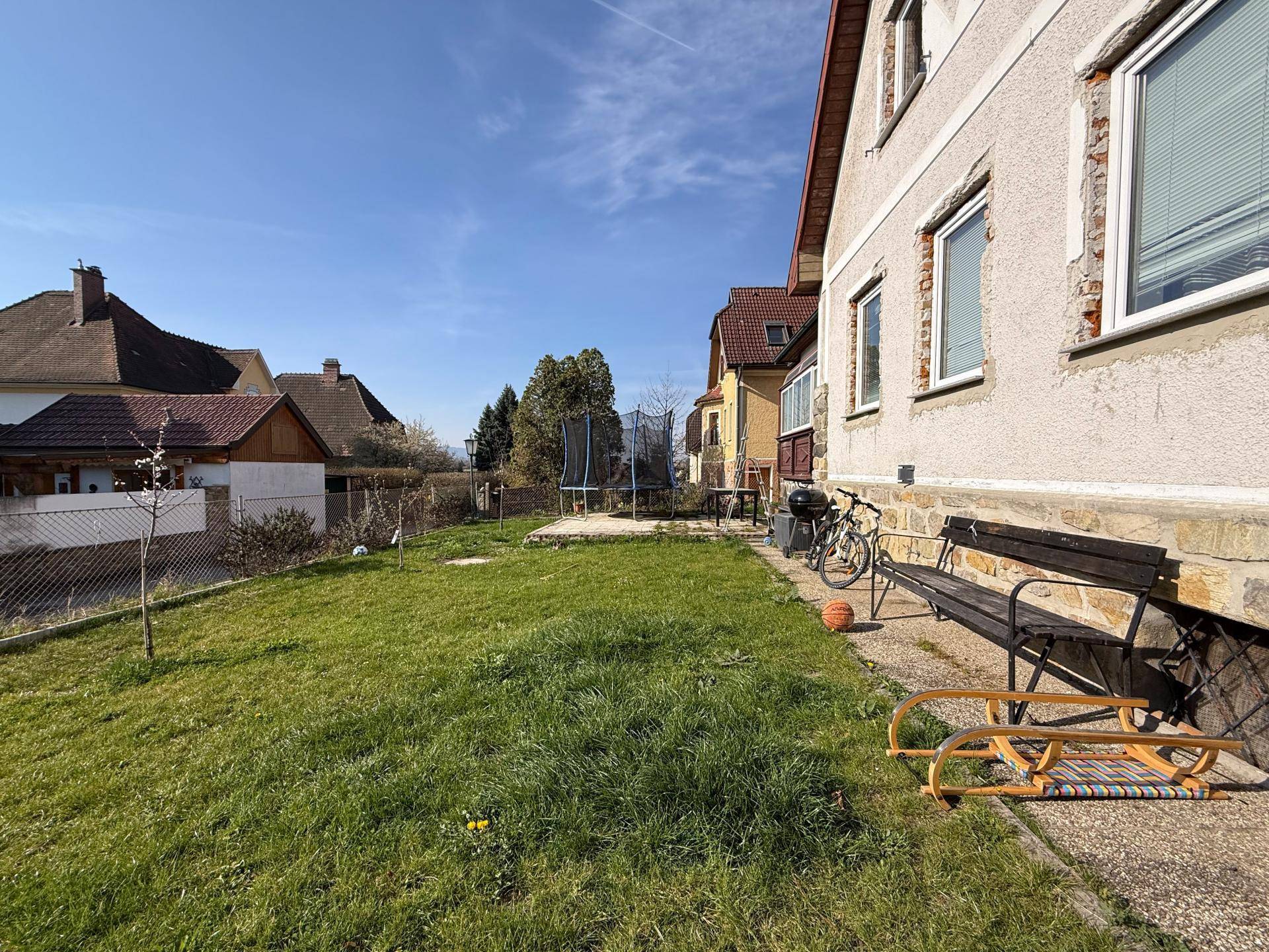 Hinterhof mit Rasenfläche, Sitzbank und Trampolin, ideal für Freizeitaktivitäten.