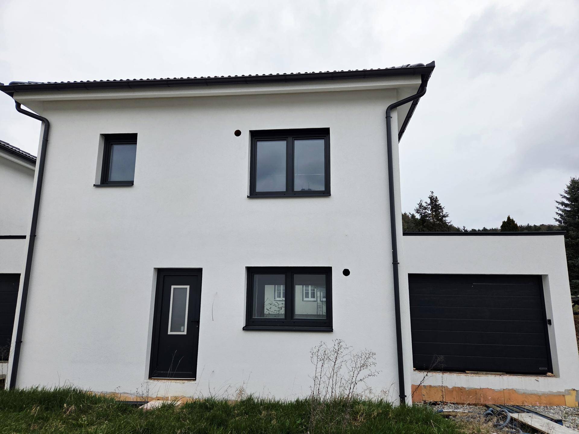 Neubau-Doppelhaushälfte mit weißer Fassade, dunklen Fenstern und integrierter Garage.