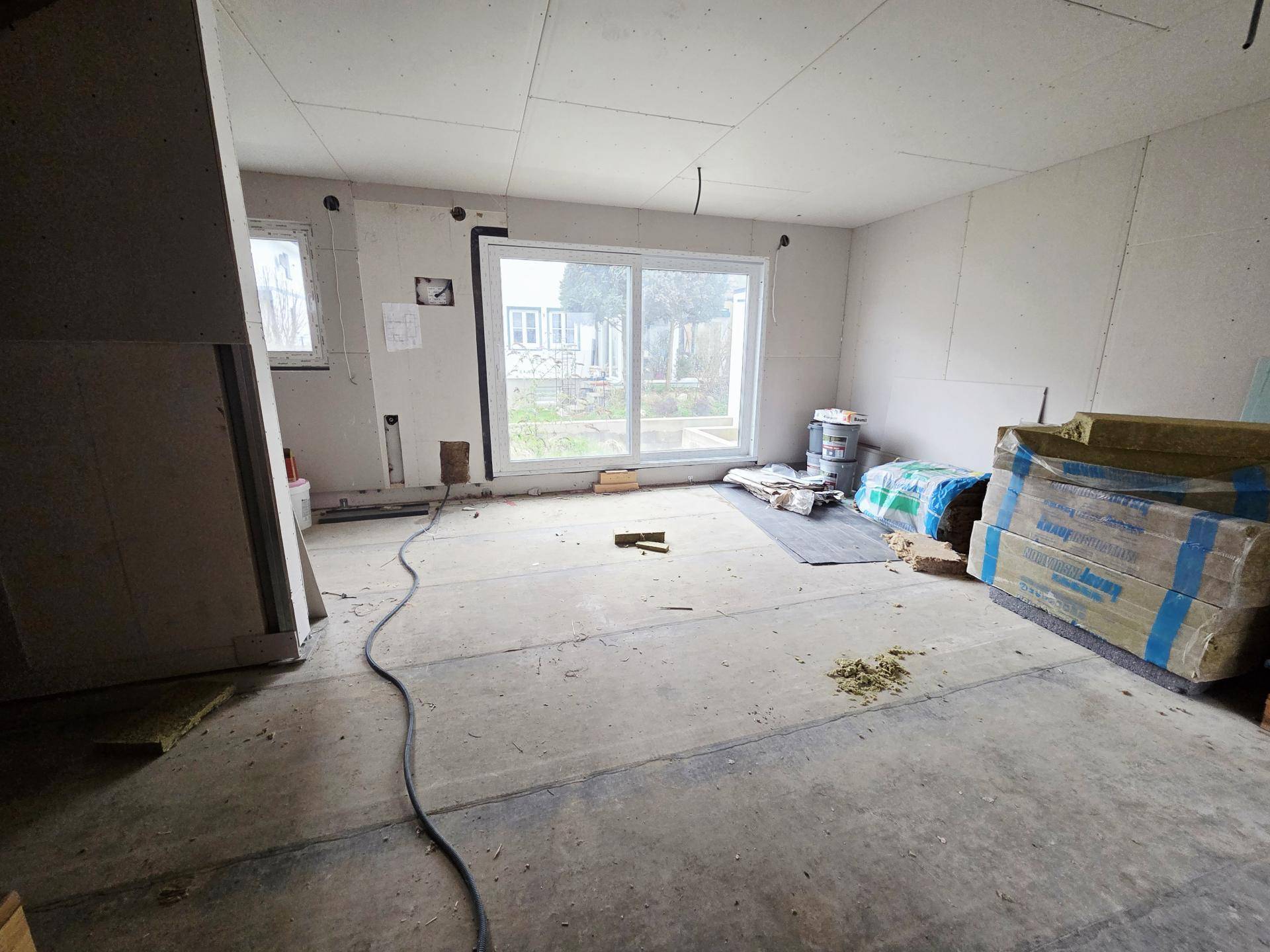 Rohbau-Wohnzimmer mit großer Fensterfront und Blick ins Grüne, bereit für den Innenausbau.