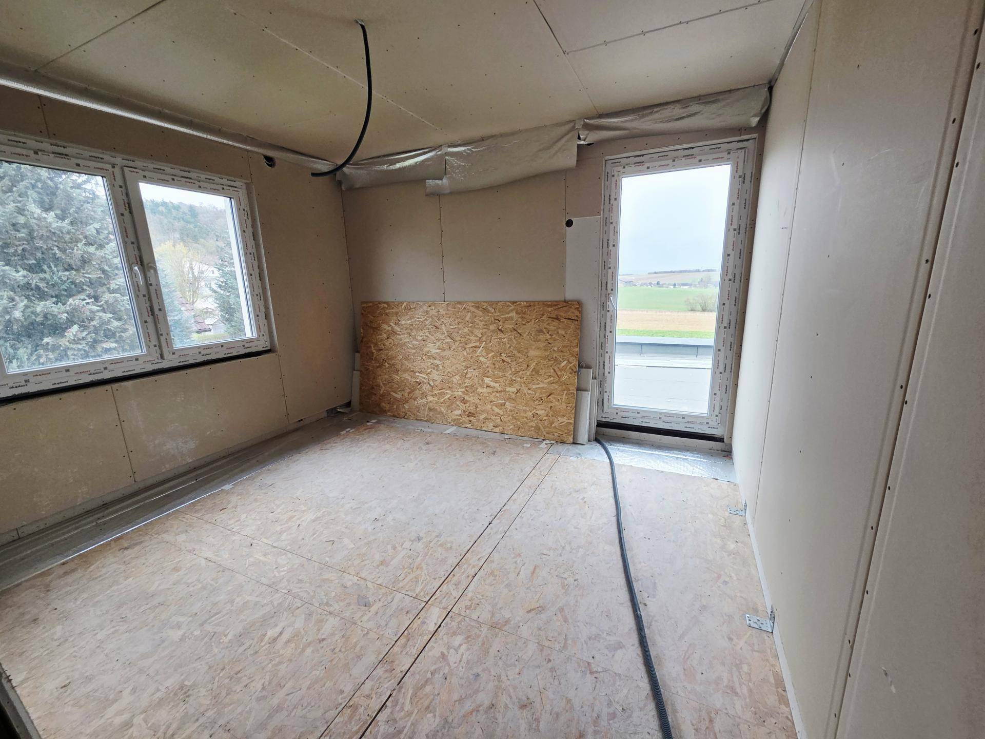 Unfertiges Zimmer mit Fenster und Tür zu einem möglichen Balkon oder einer Terrasse im Neubau.