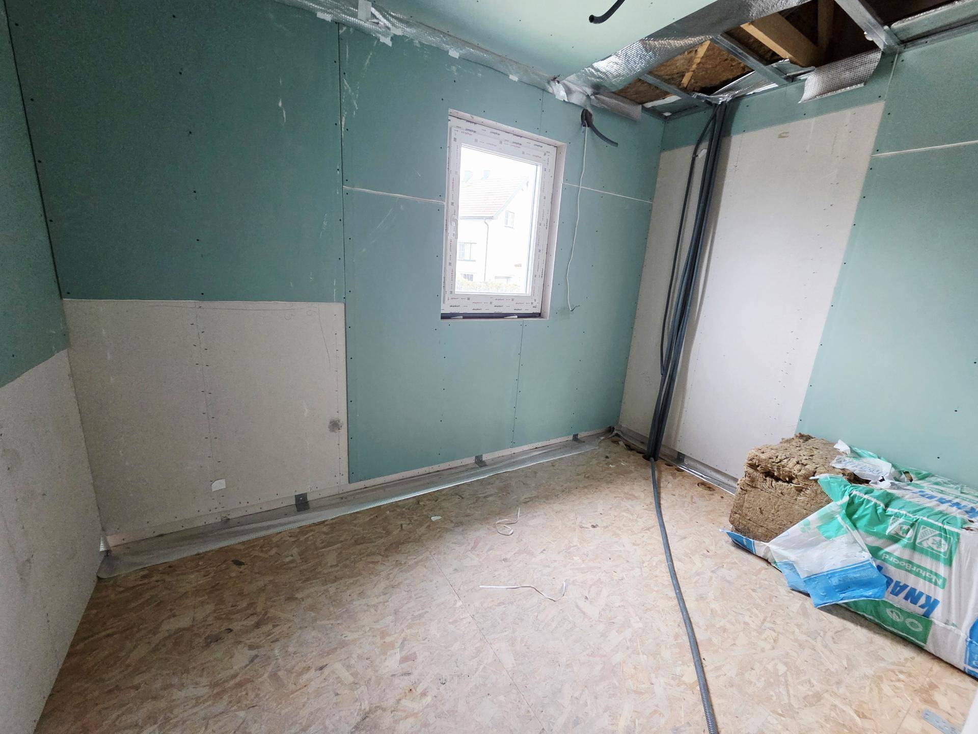 Rohbau-Zimmer mit Trockenbauwänden und einem Fenster, bereit für den weiteren Innenausbau.