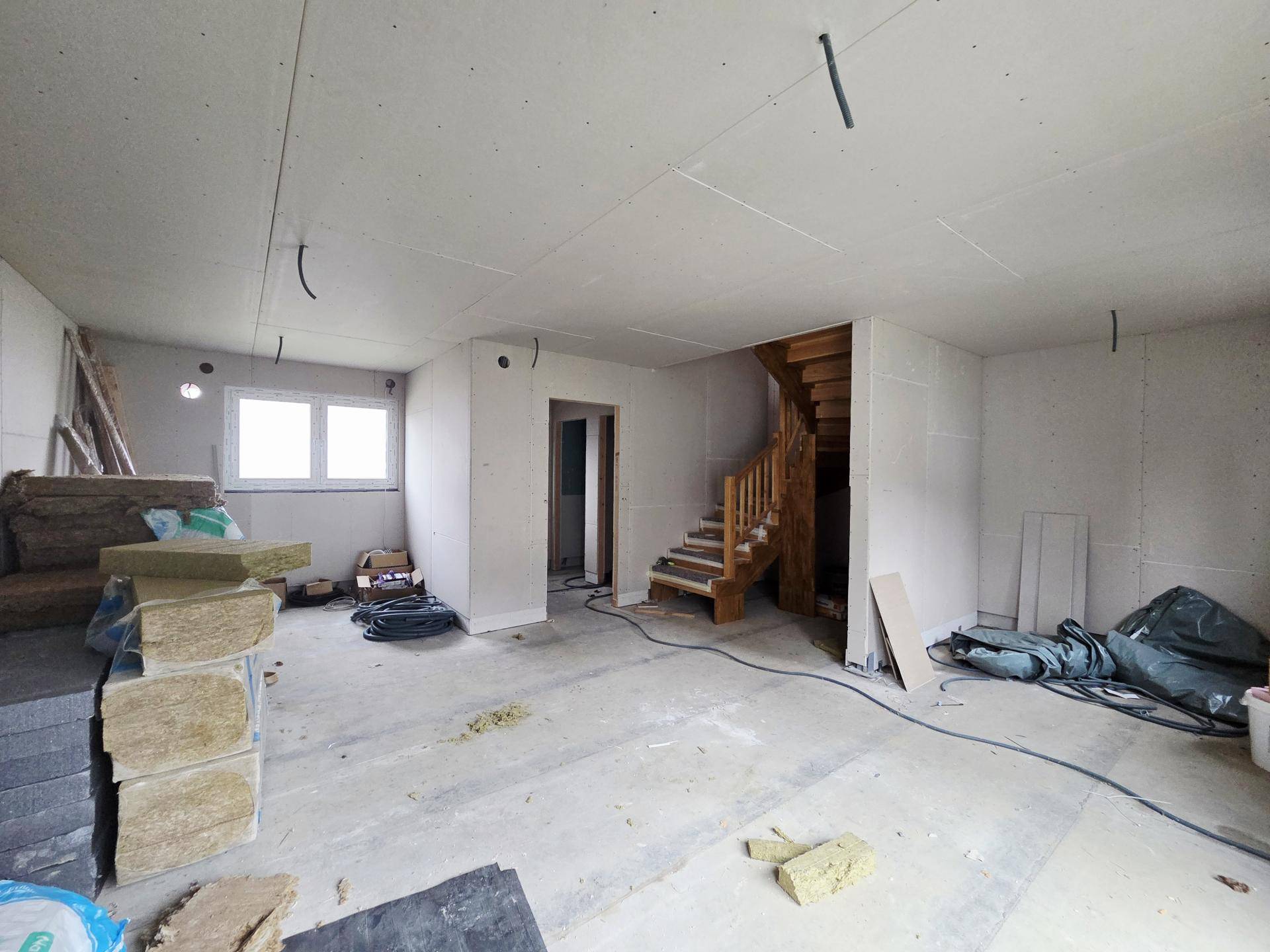 Großer Rohbau-Raum mit offener Holztreppe und viel Potenzial für die individuelle Gestaltung.
