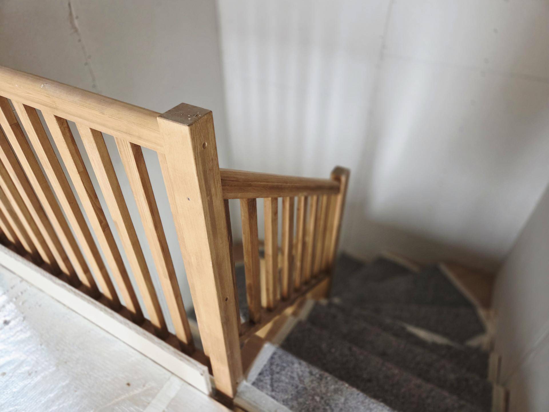 Holzgeländer einer Treppe mit Steinstufen, die in ein höheres Stockwerk des Neubaus führt.