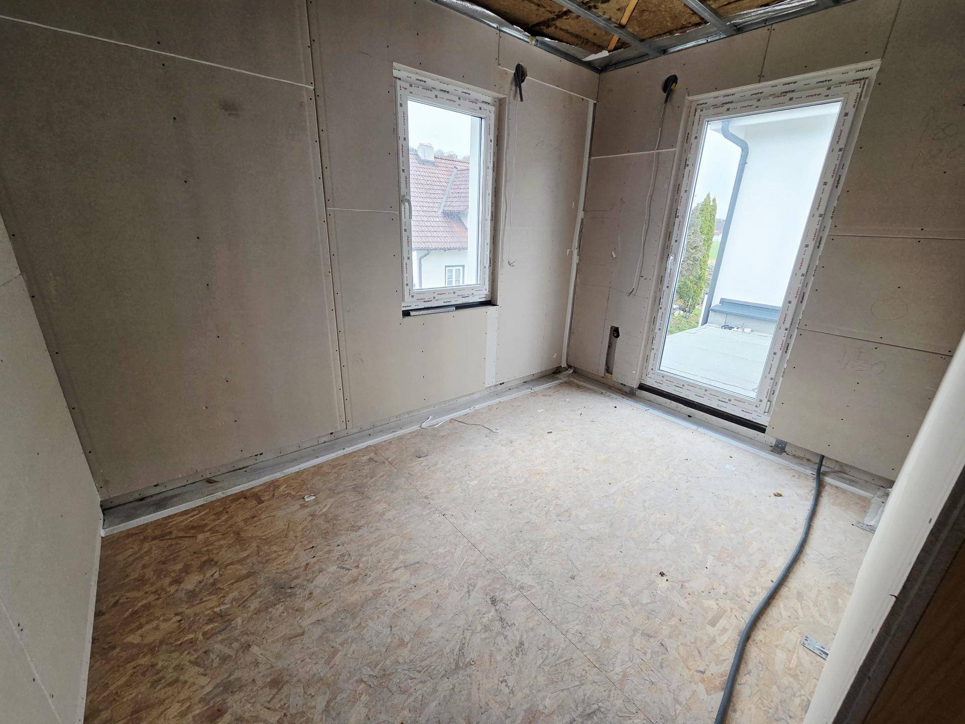 Schlafzimmer im Rohbau mit OSB-Plattenboden, Trockenbauwänden und Zugang zu einem Außenbereich.