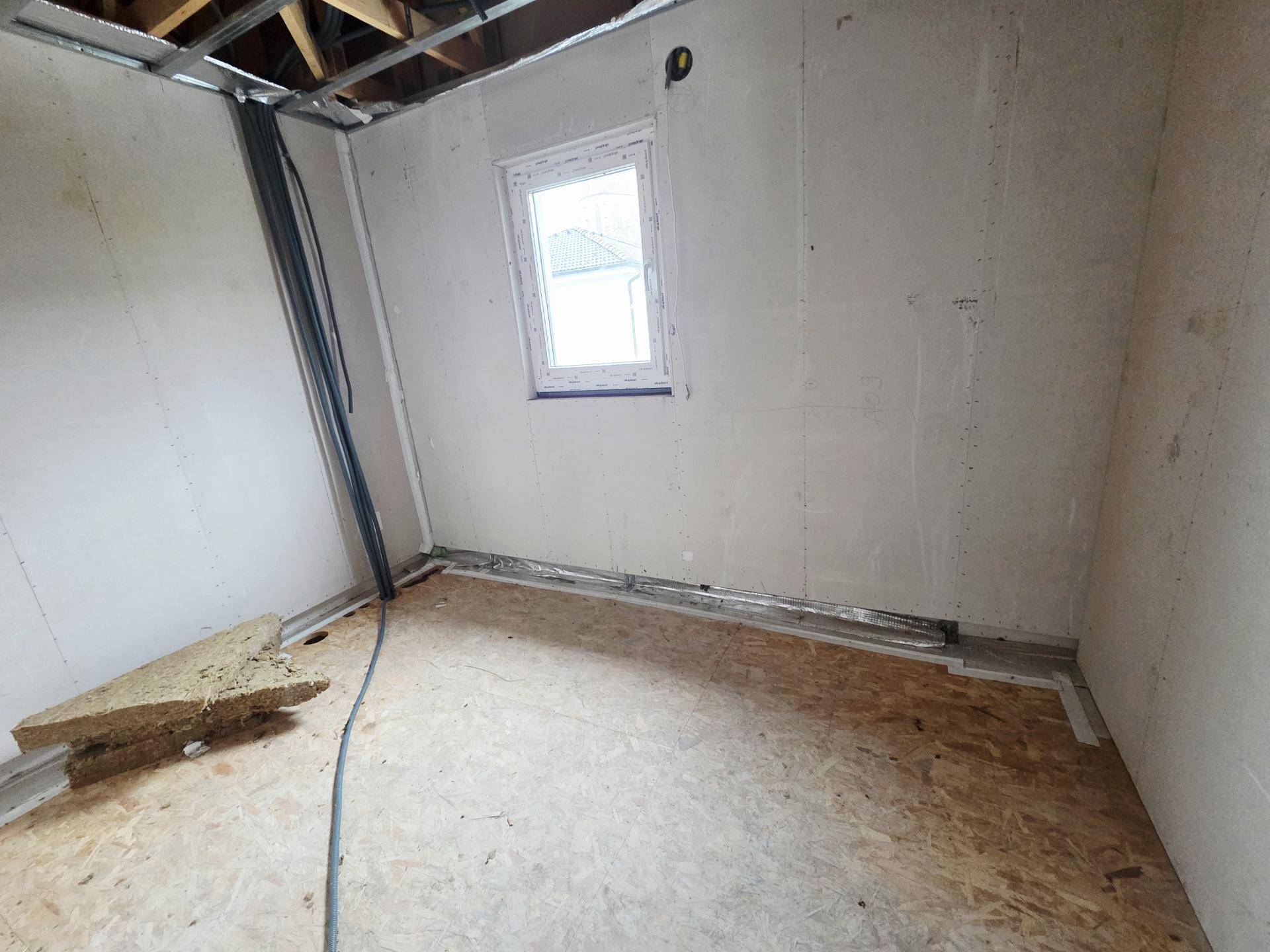 Schlafzimmer im Rohbau mit OSB-Plattenboden, Trockenbauwänden, Fenster und sichtbaren Elektroleitungen.