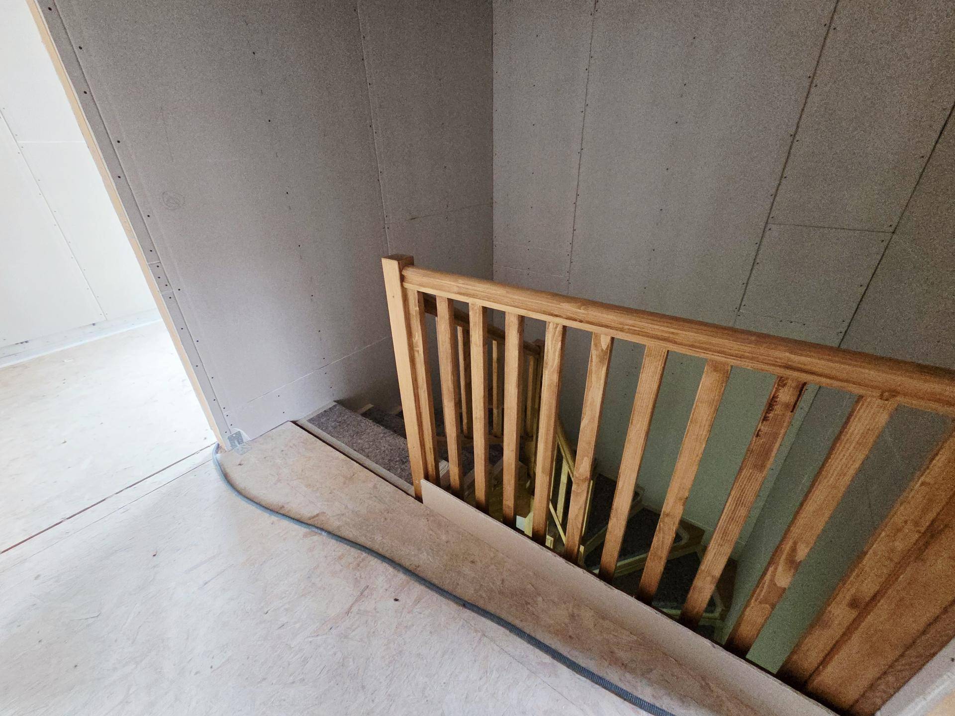 Treppenbereich im Rohbau mit einem einfachen Holzgeländer und Trockenbauwänden.