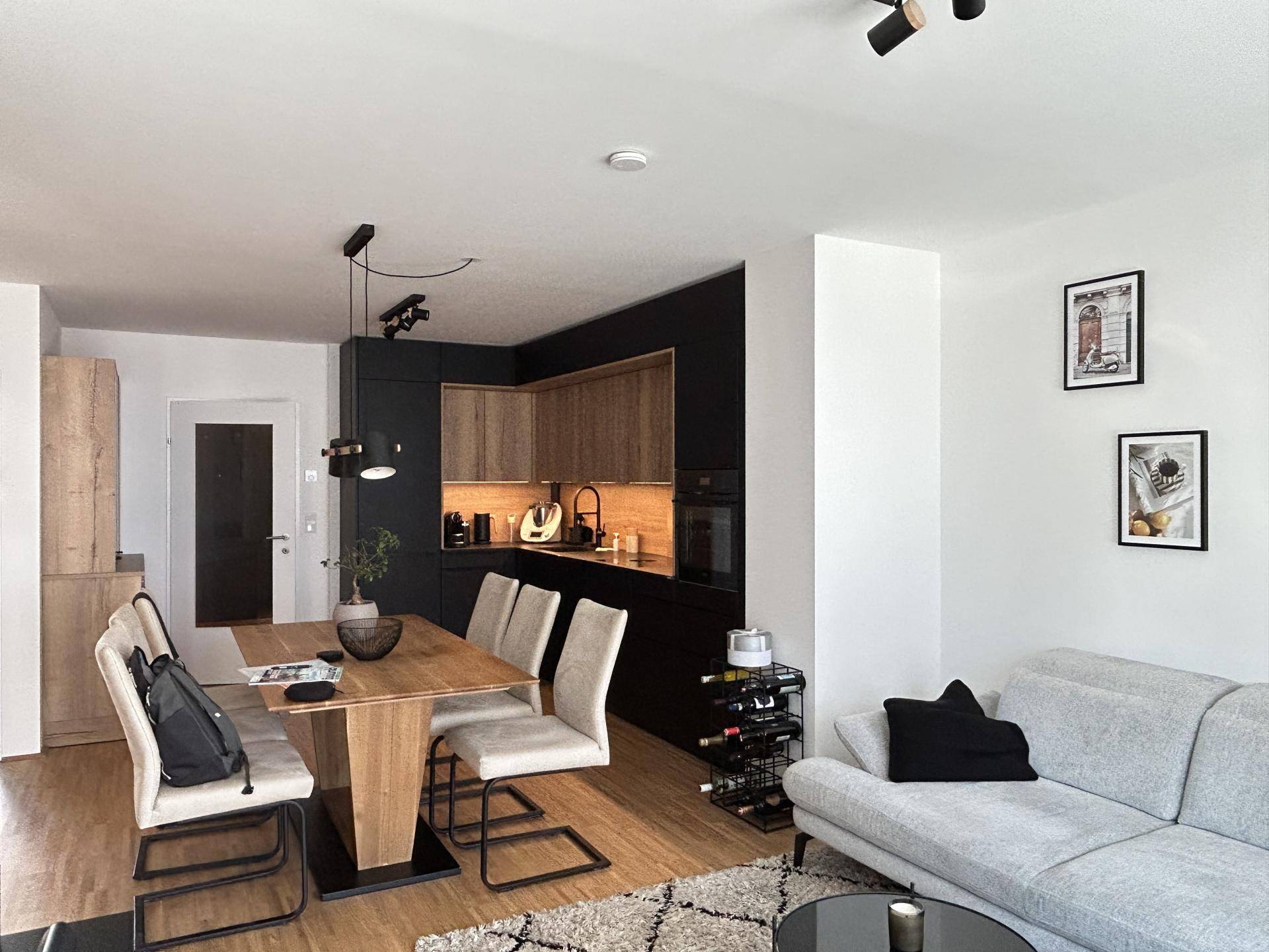 Offener Wohn- und Essbereich mit moderner Küche, Holztisch und bequemer Couch.