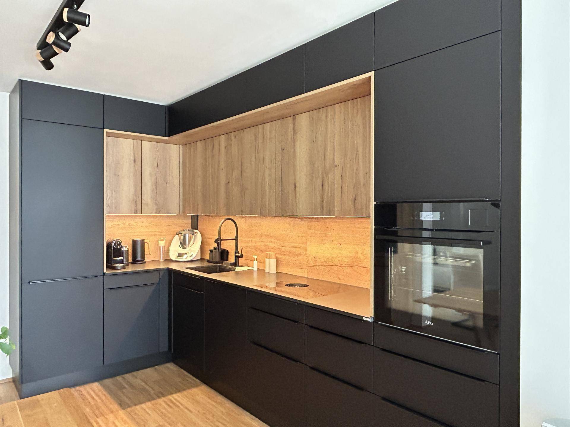 Moderne Küche mit schwarzen und holzfarbenen Schränken, integrierten Geräten und Arbeitsplatte.