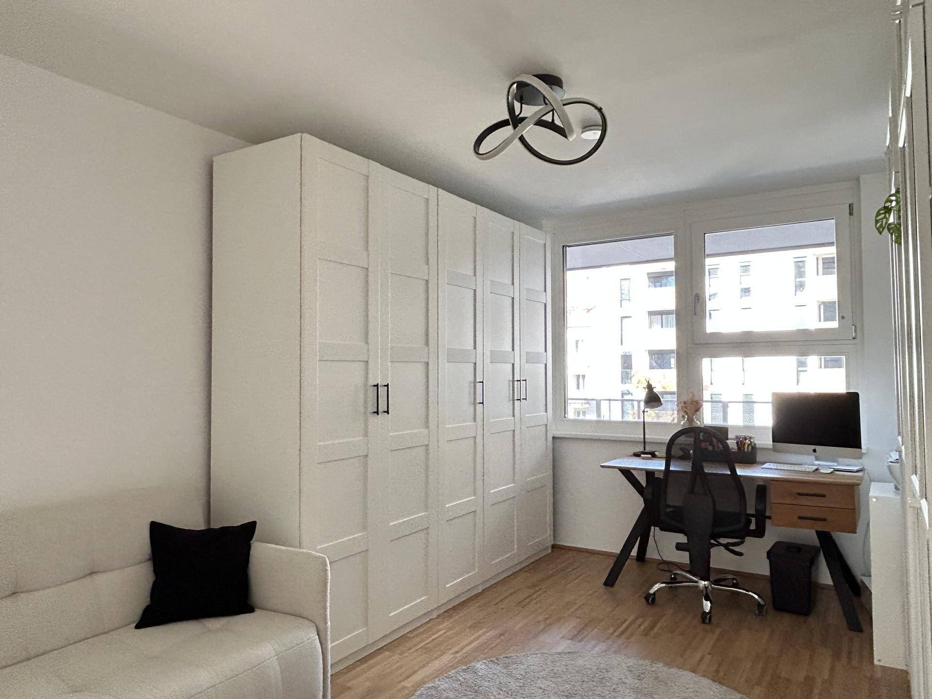 Helles Arbeitszimmer mit großem Fenster, Einbauschränken und Holzboden.