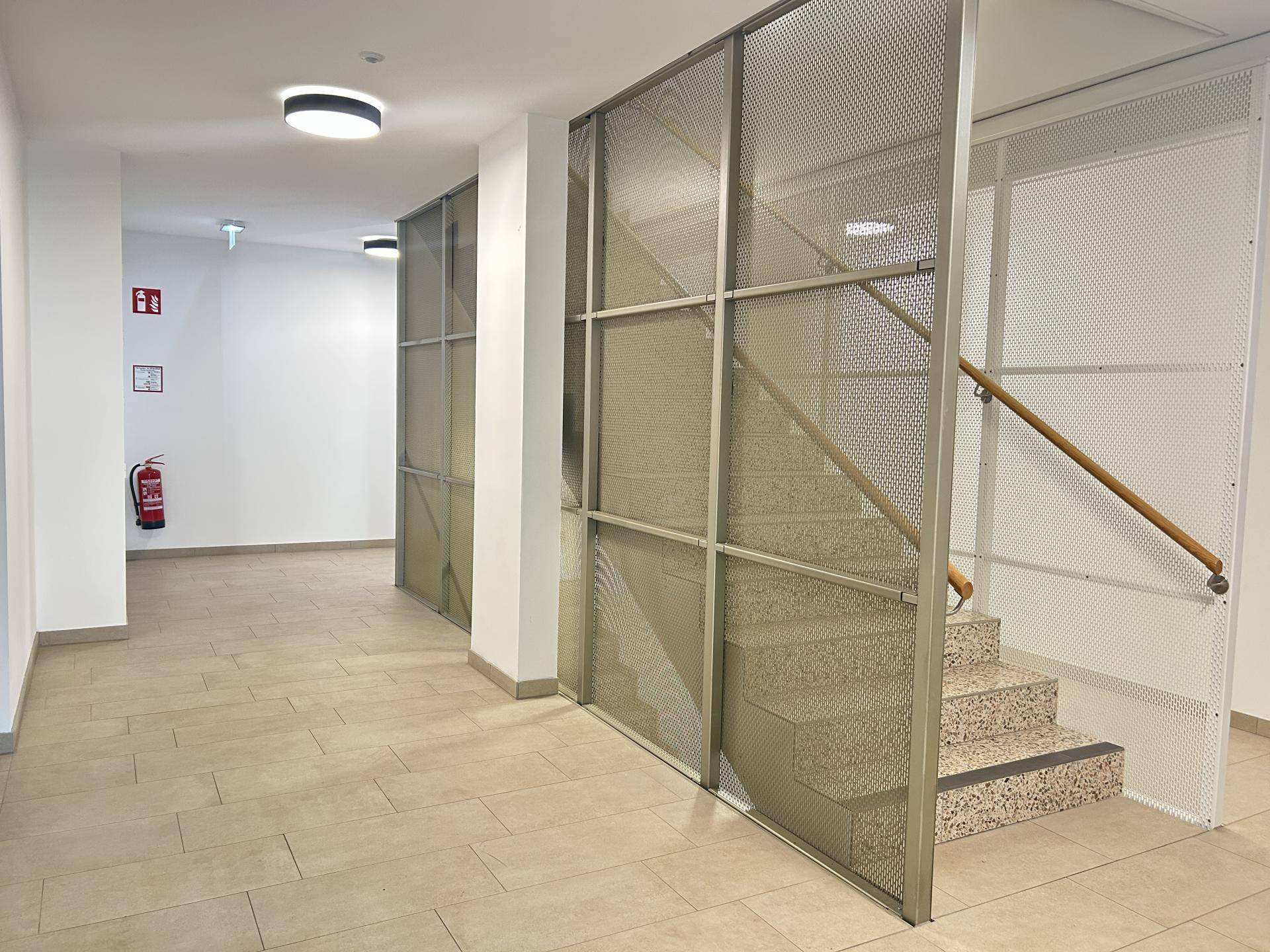 Heller Flur im Gebäude mit Treppenhaus und Fliesenboden.