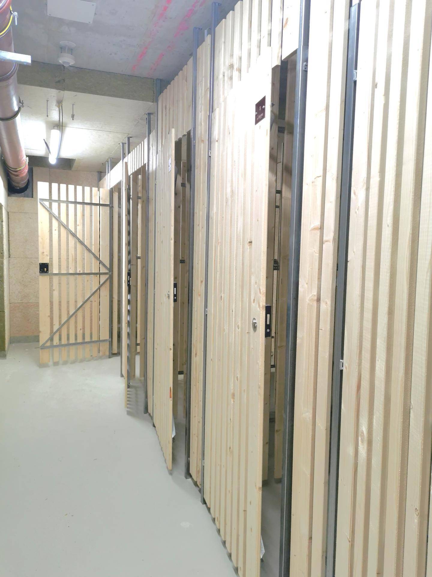 Reihen von Lagerräumen im Kellerbereich mit Holztüren und Betonboden.