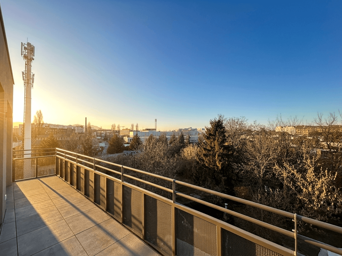 Großer Balkon mit Weitblick über die Stadt und umliegende Bäume bei Sonnenuntergang.