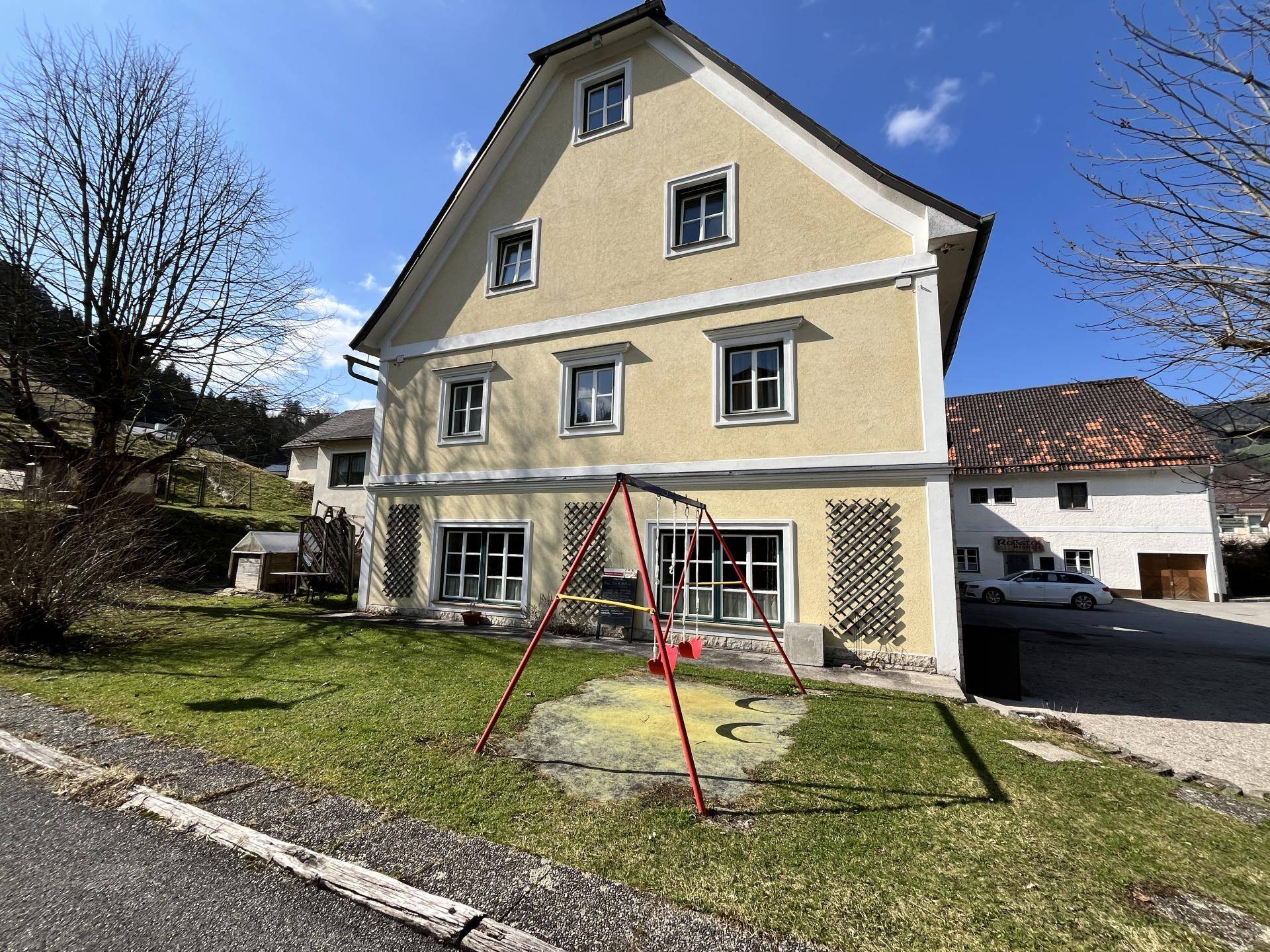 Rückseite des Gebäudes mit einem grünen Garten und einem Kinderspielplatz.