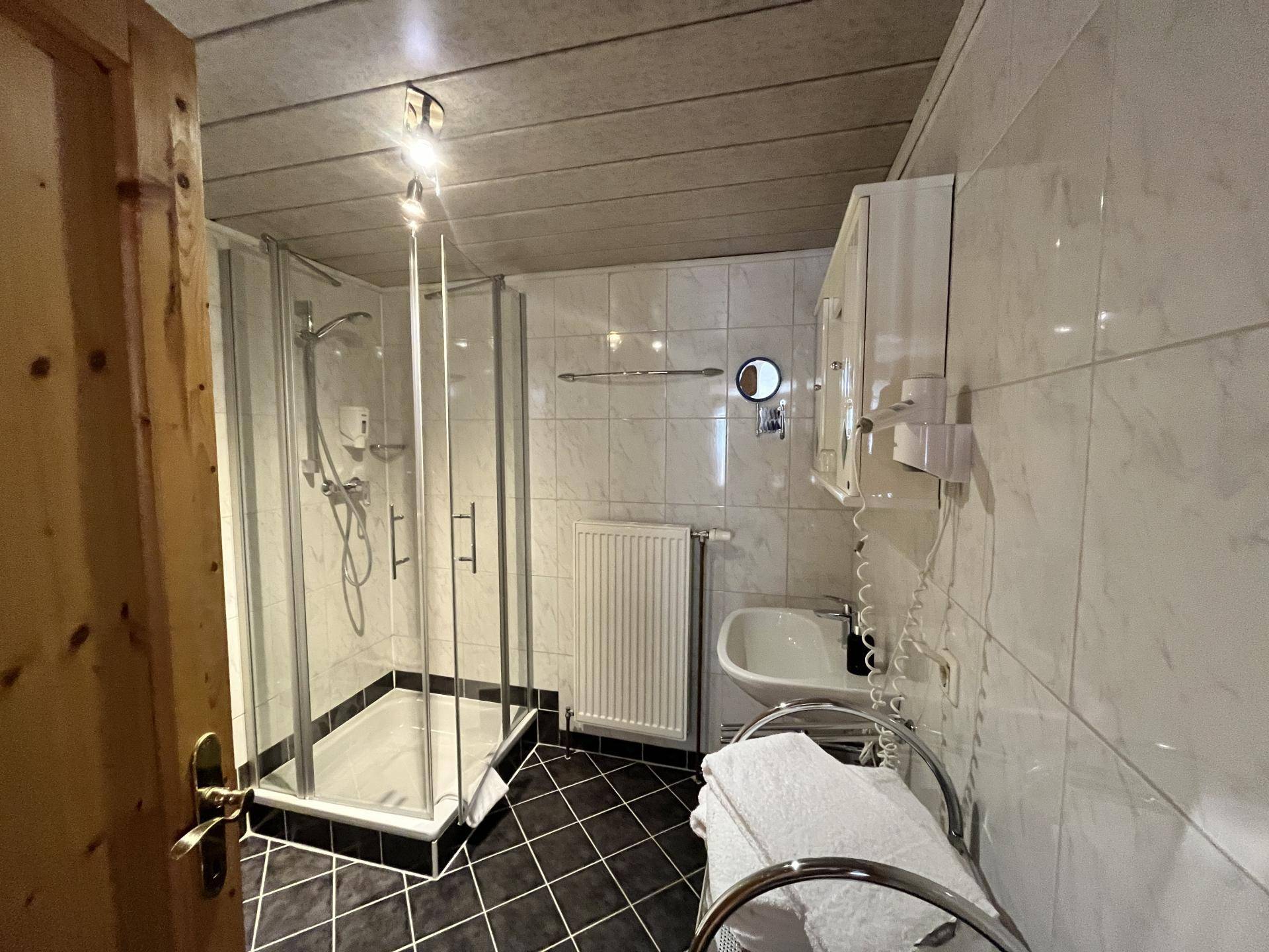 Kleines Badezimmer mit Duschkabine, Waschbecken und dunklen Bodenfliesen.