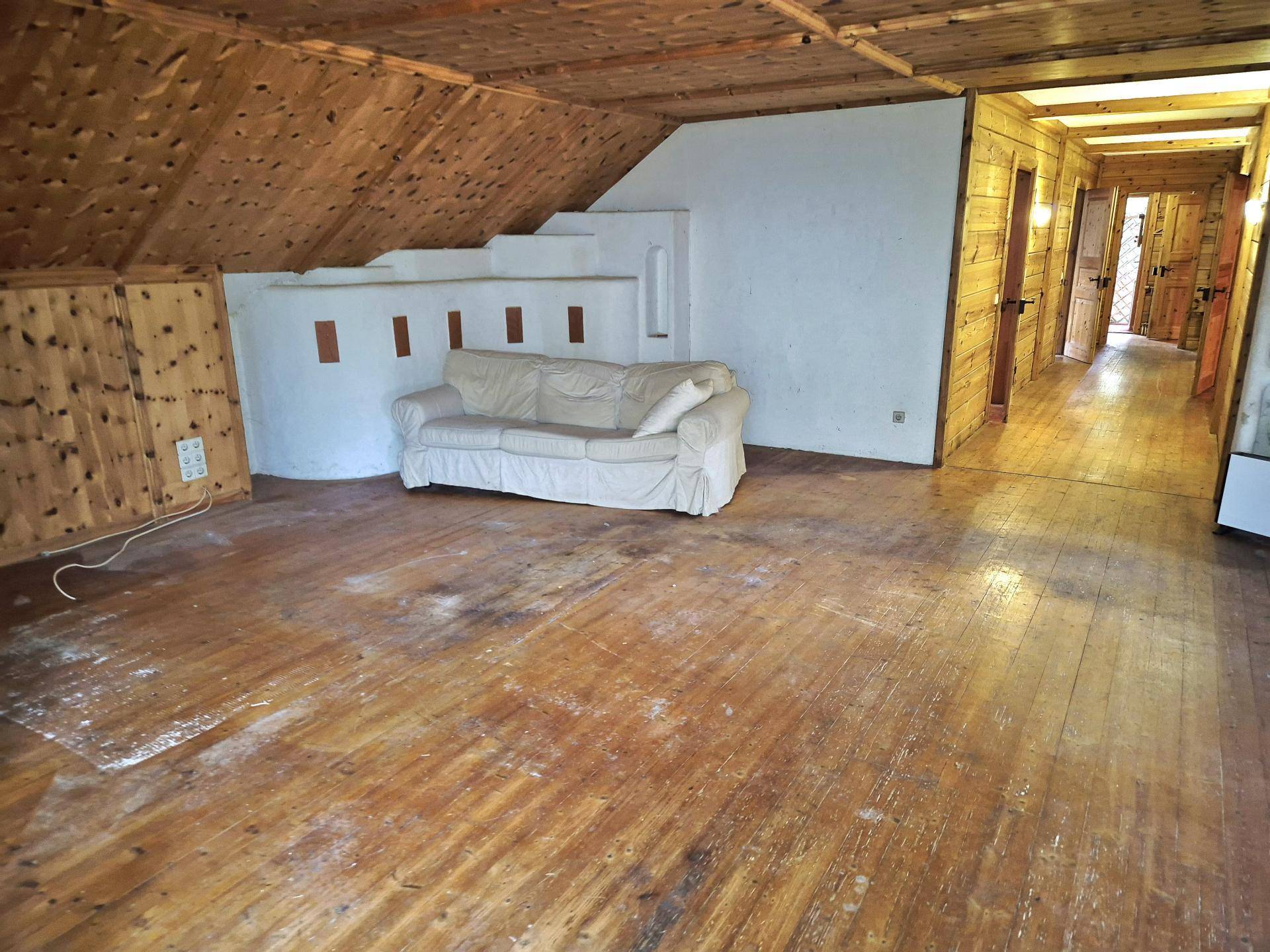 Großer Wohnbereich im Dachgeschoss mit Holzboden, Holzverkleidung und Sofa.