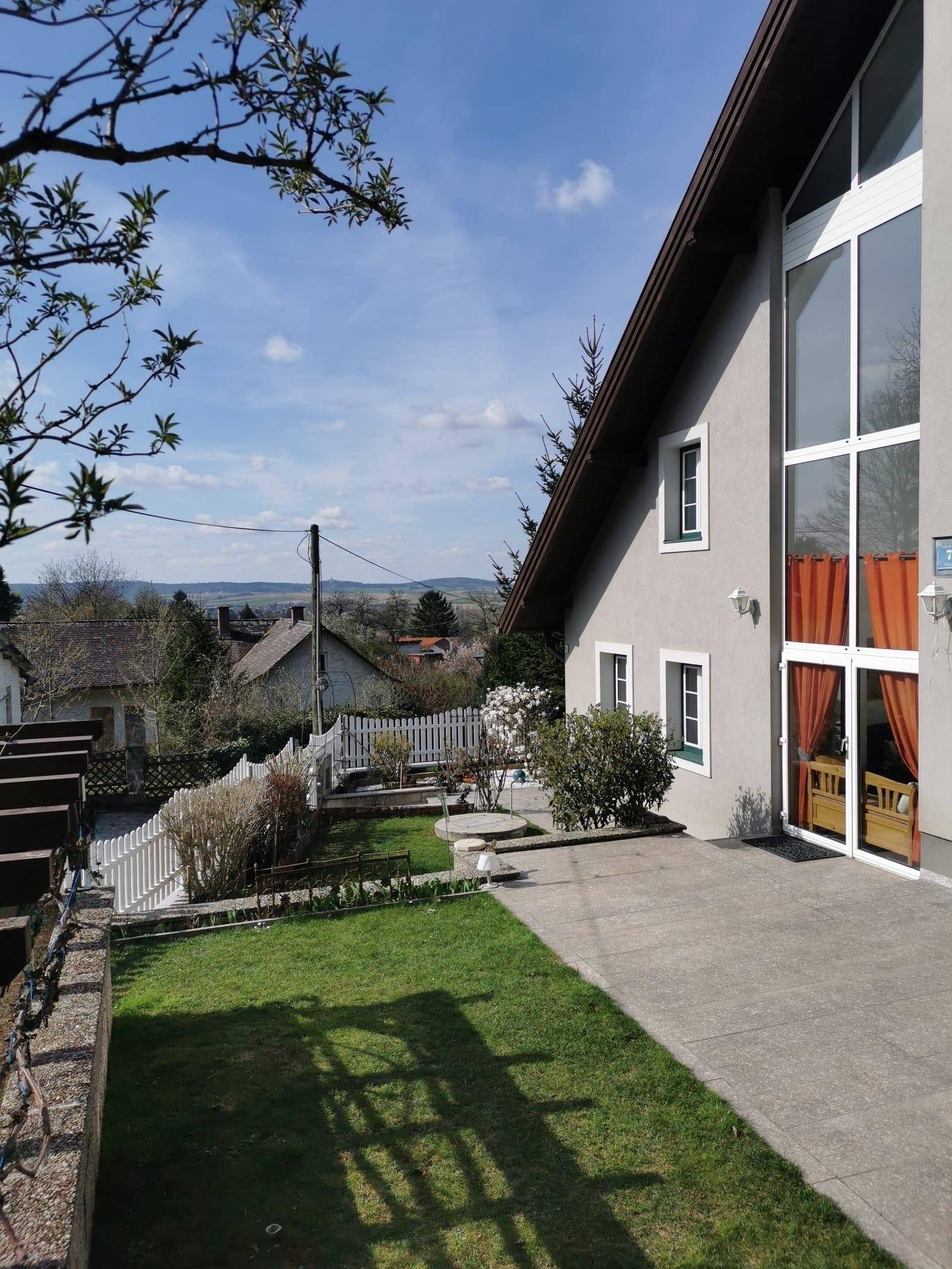 Seitlicher Gartenbereich mit gepflastertem Weg, Rasenfläche und weitem Blick in die Landschaft.