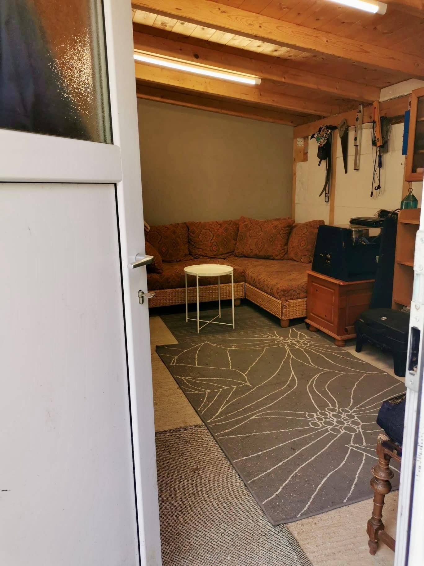 Gemütlicher Wohnbereich mit großem Sofa, Teppich und sichtbaren Holzdeckenbalken, der auch als Werkstatt dient.