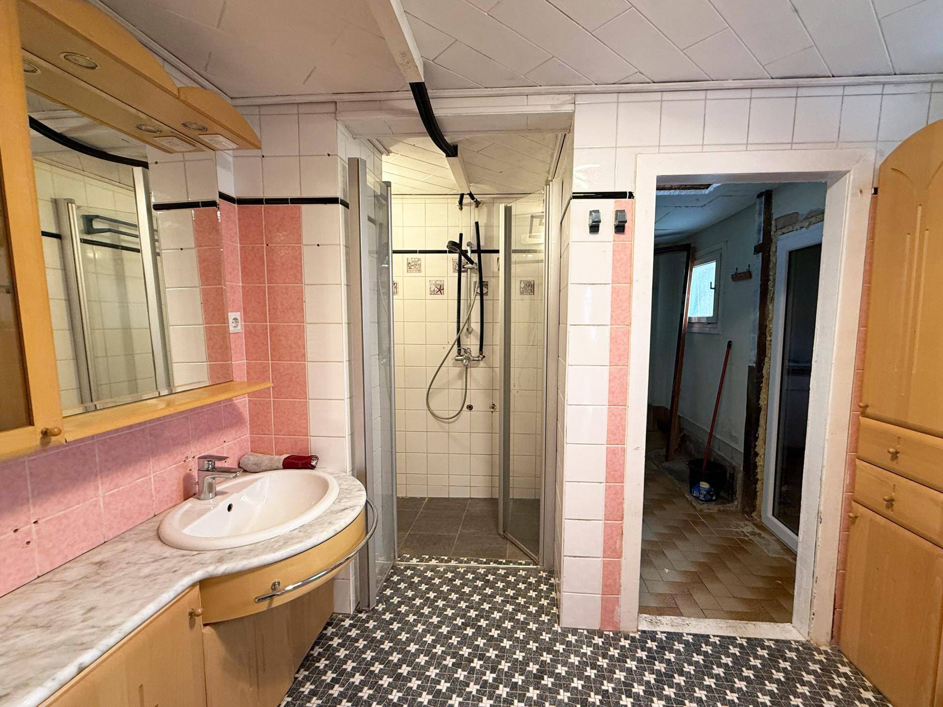 Badezimmer mit rosa und weißen Fliesen, Einzelwaschbecken und einer Duschkabine.