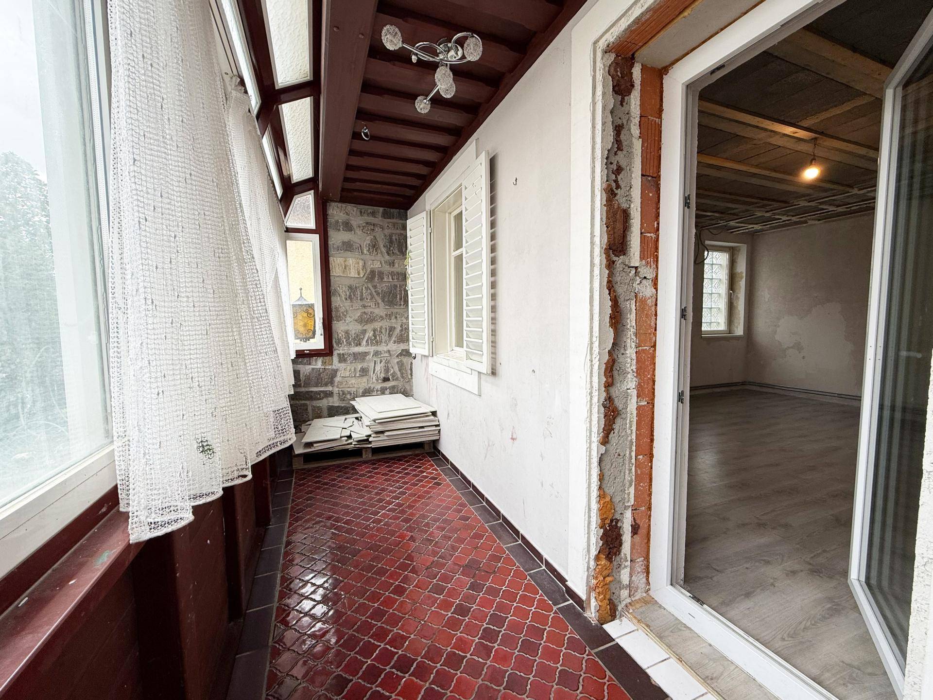 Verglaste Loggia mit roten Fliesen und Blick nach draußen, ideal als geschützter Außenbereich.