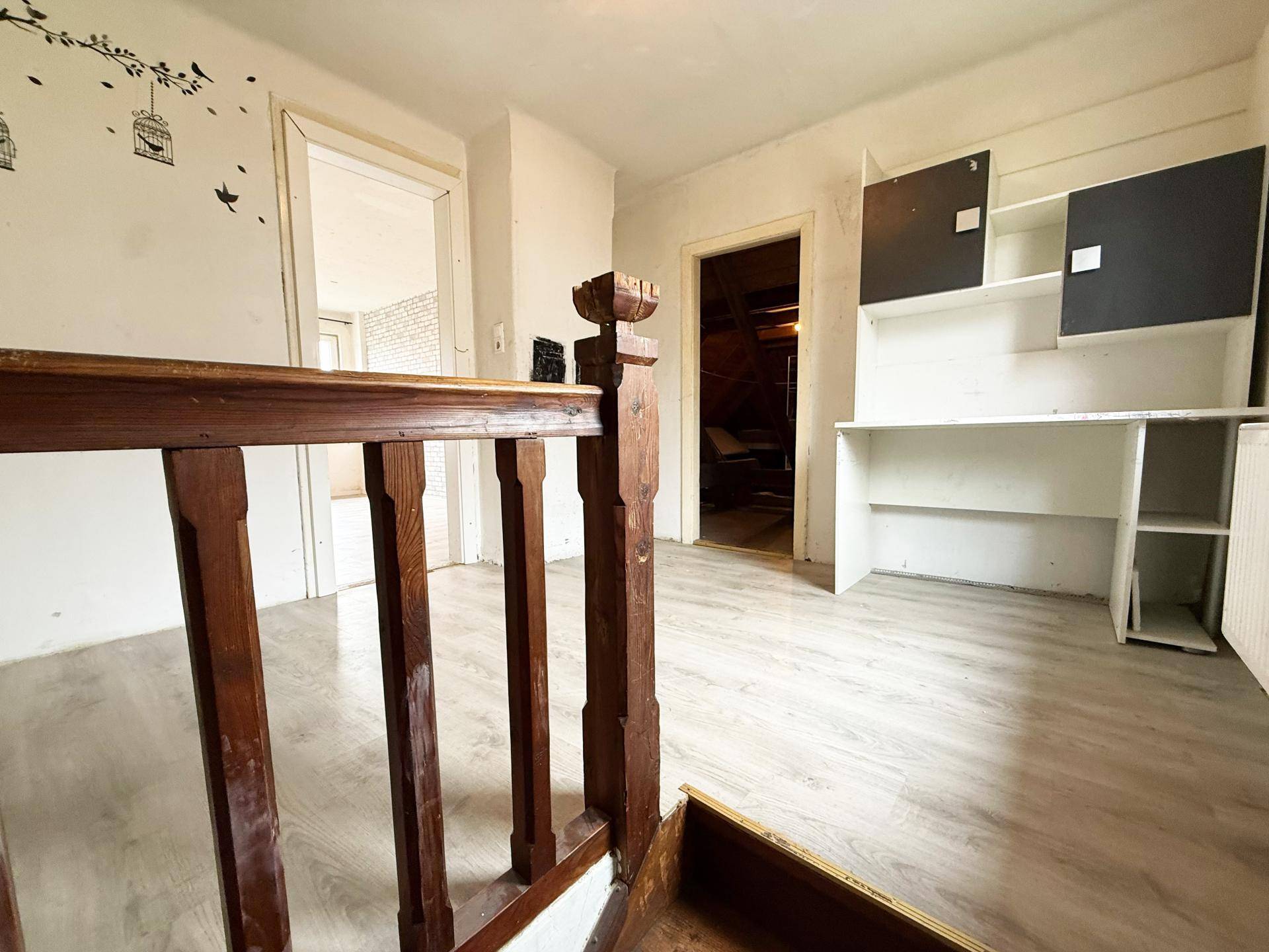 Oberer Flurbereich mit Laminatboden, Holzgeländer und einem Einbauschrank, der zu weiteren Räumen führt.