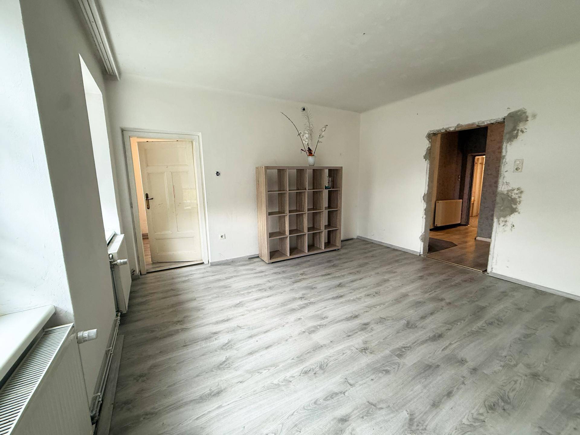 Helles Wohnzimmer mit Laminatboden und einem offenen Regal, bereit für individuelle Gestaltung.