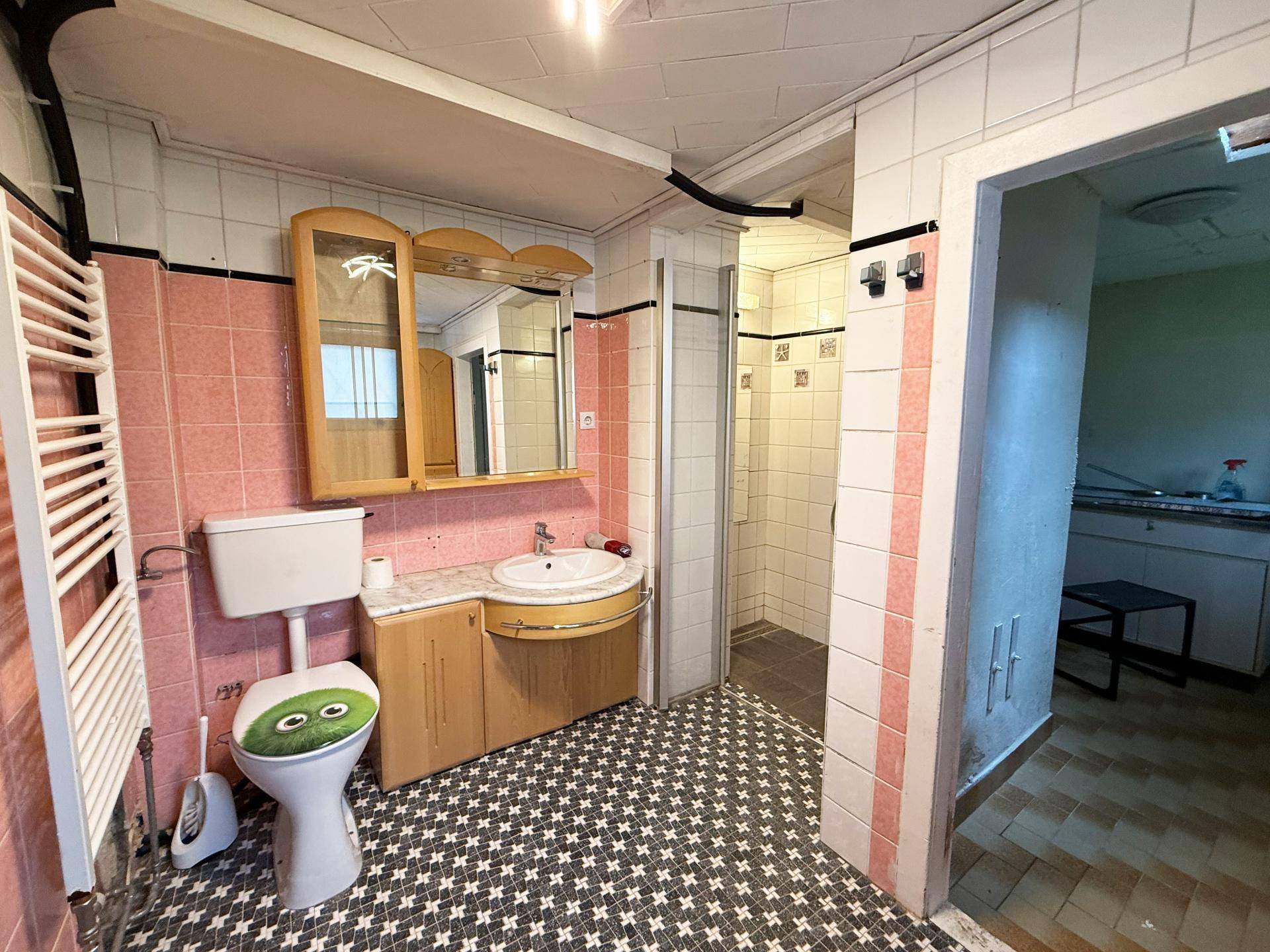 Badezimmer mit rosa und weißen Fliesen, WC, Waschbecken und Duschbereich, in älterem Zustand.