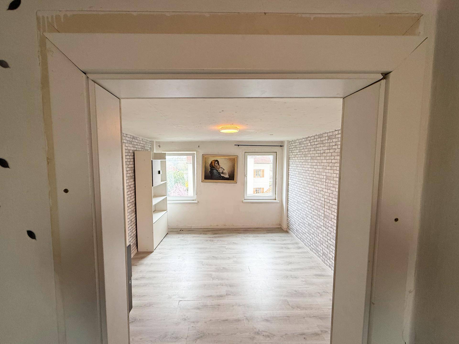 Blick durch einen Türrahmen in ein Schlafzimmer mit Laminatboden und Ziegeloptik-Tapete.