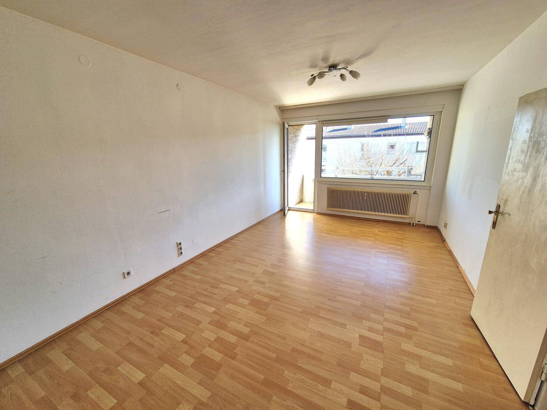 Helles Wohnzimmer mit Laminatboden und Zugang zu einem Balkon, ideal für entspannte Stunden.