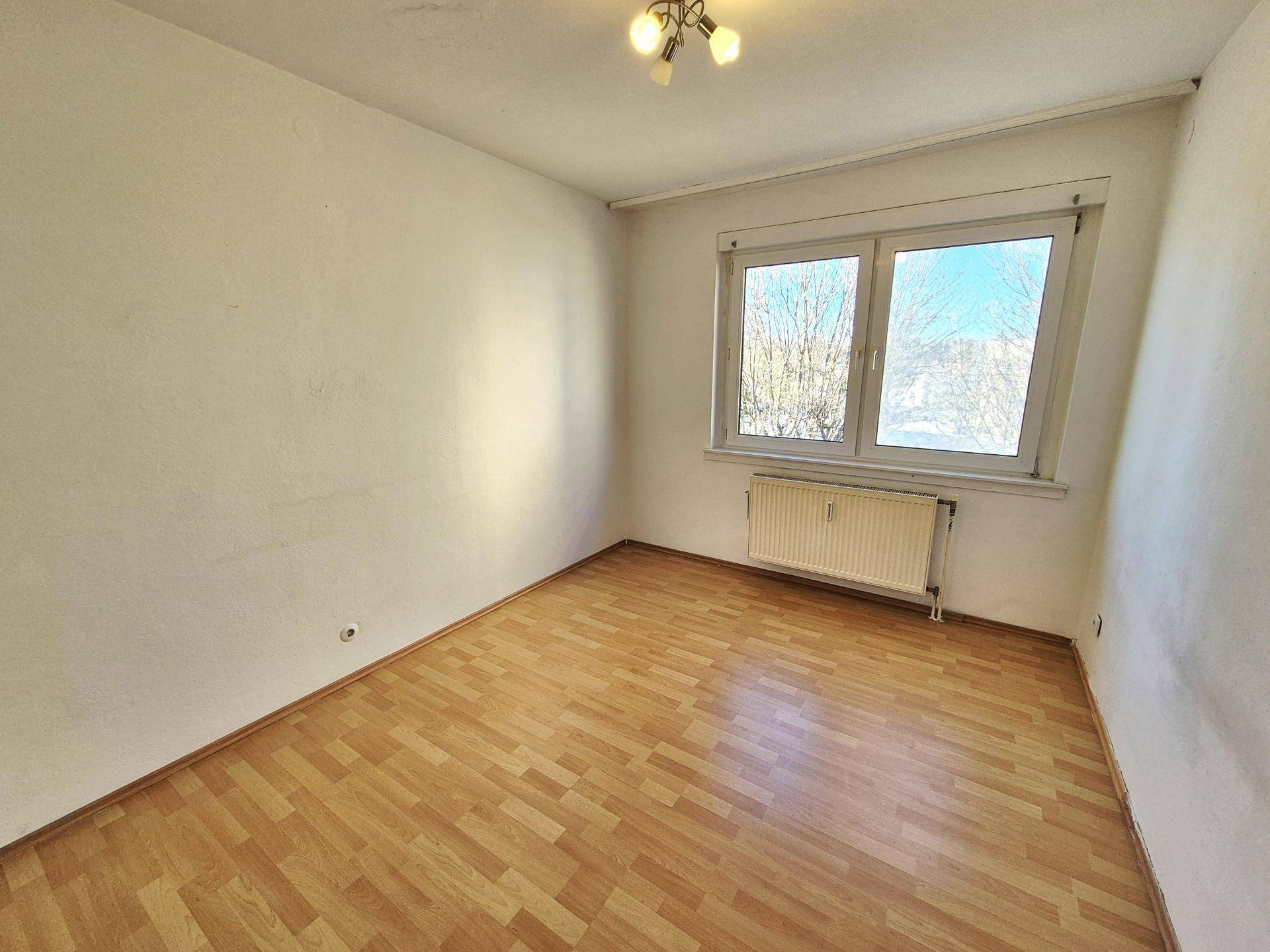 Helles Schlafzimmer mit Laminatboden und Ausblick ins Grüne durch das Fenster.