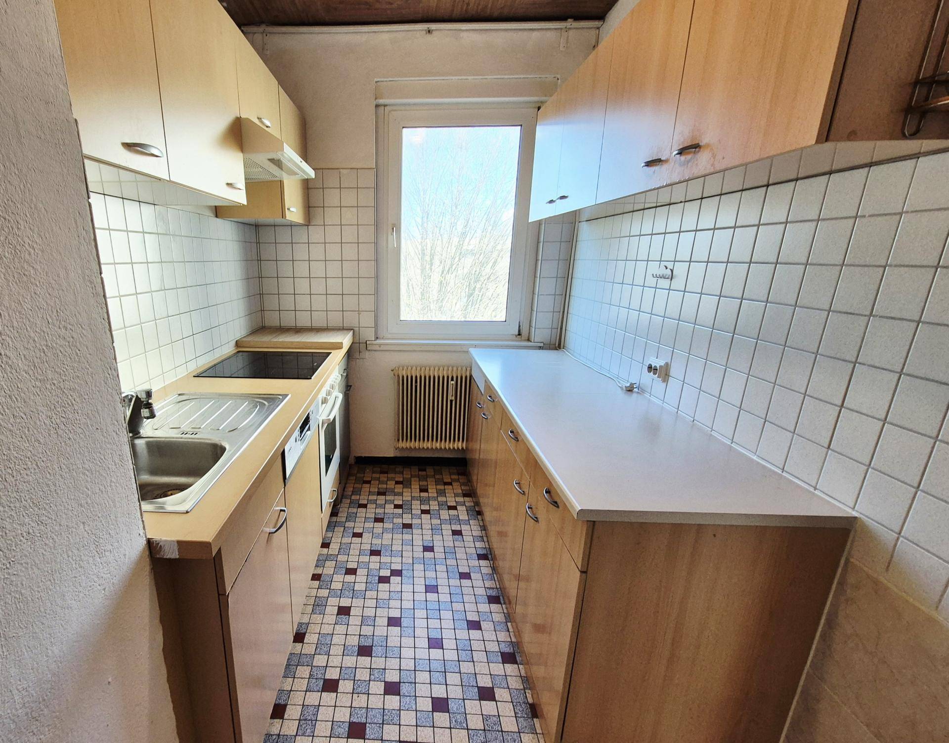 Funktionale Küche mit hellen Holzschränken, Fliesenboden und Fenster mit Ausblick.