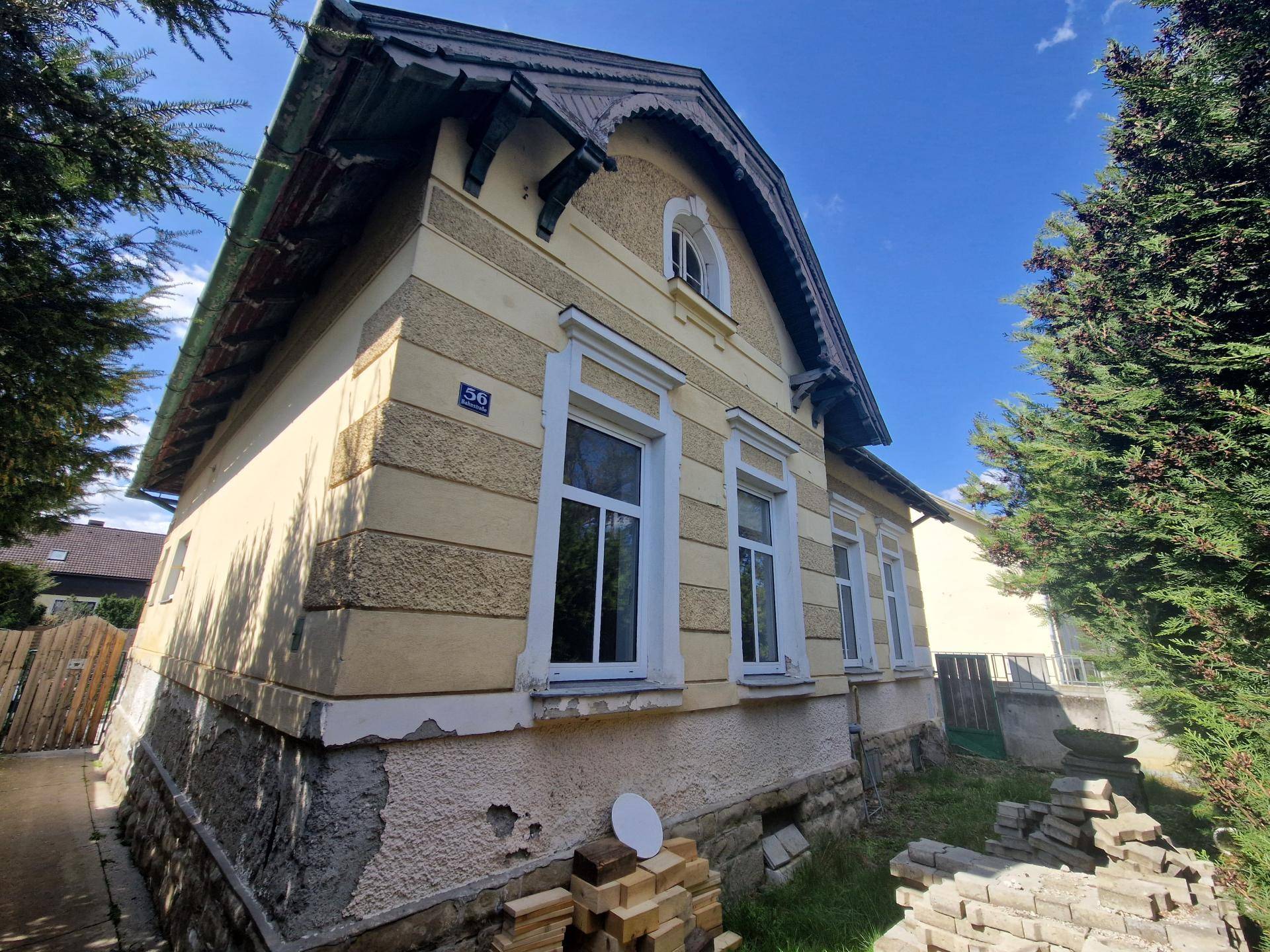 Seitenansicht des Hauses mit gelber Fassade, weißen Fenstern und sichtbaren Fundamenten.