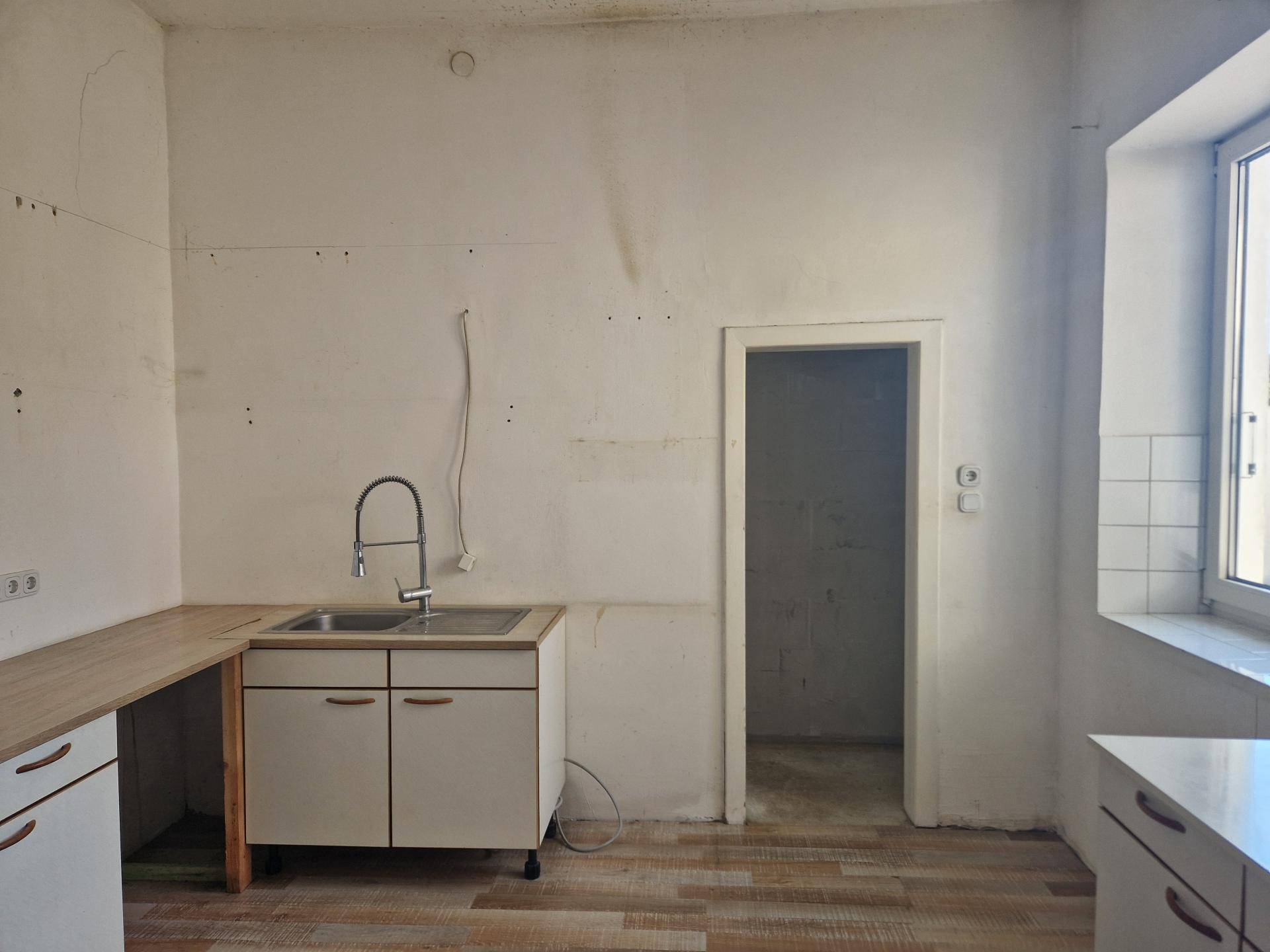 Einfache Küche mit Spülbecken, Arbeitsplatte und Fliesen an der Wand, bereit zur Renovierung.