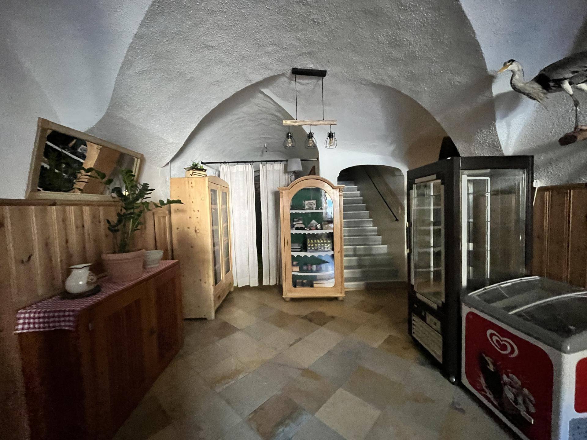 Gewölbter Innenraum mit Steinboden, Vitrinen und Kühlgeräten, führt zu einer Treppe.