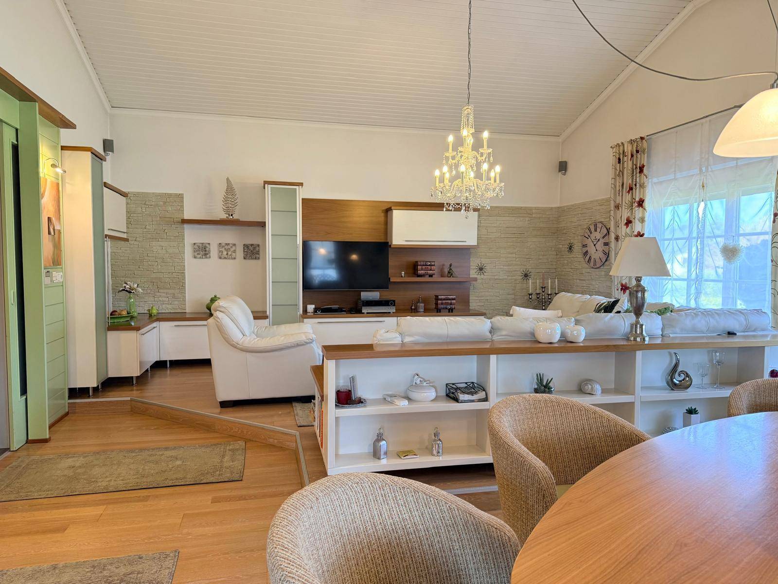 Geräumiges Wohnzimmer mit hohen Decken, Parkettboden und großem Sofa unter einem Kronleuchter.