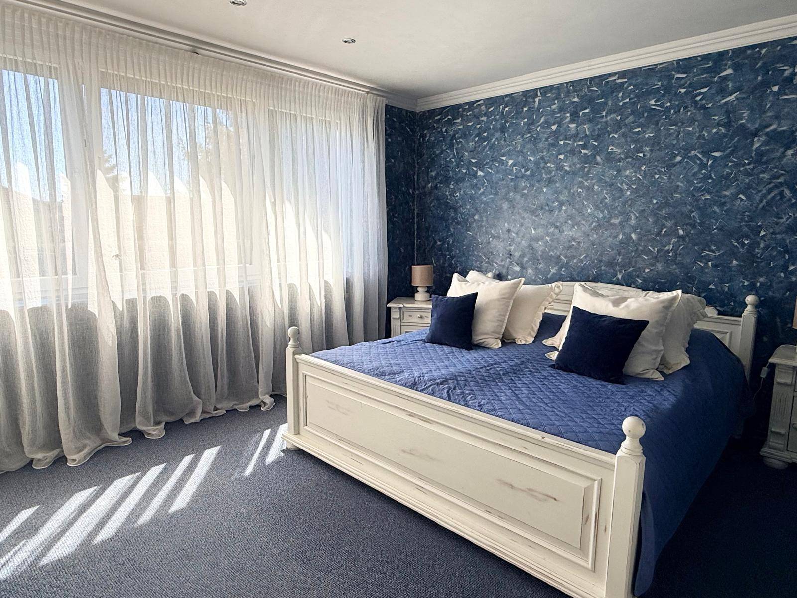 Helles Schlafzimmer mit Doppelbett, blauer Wandgestaltung und Teppichboden.