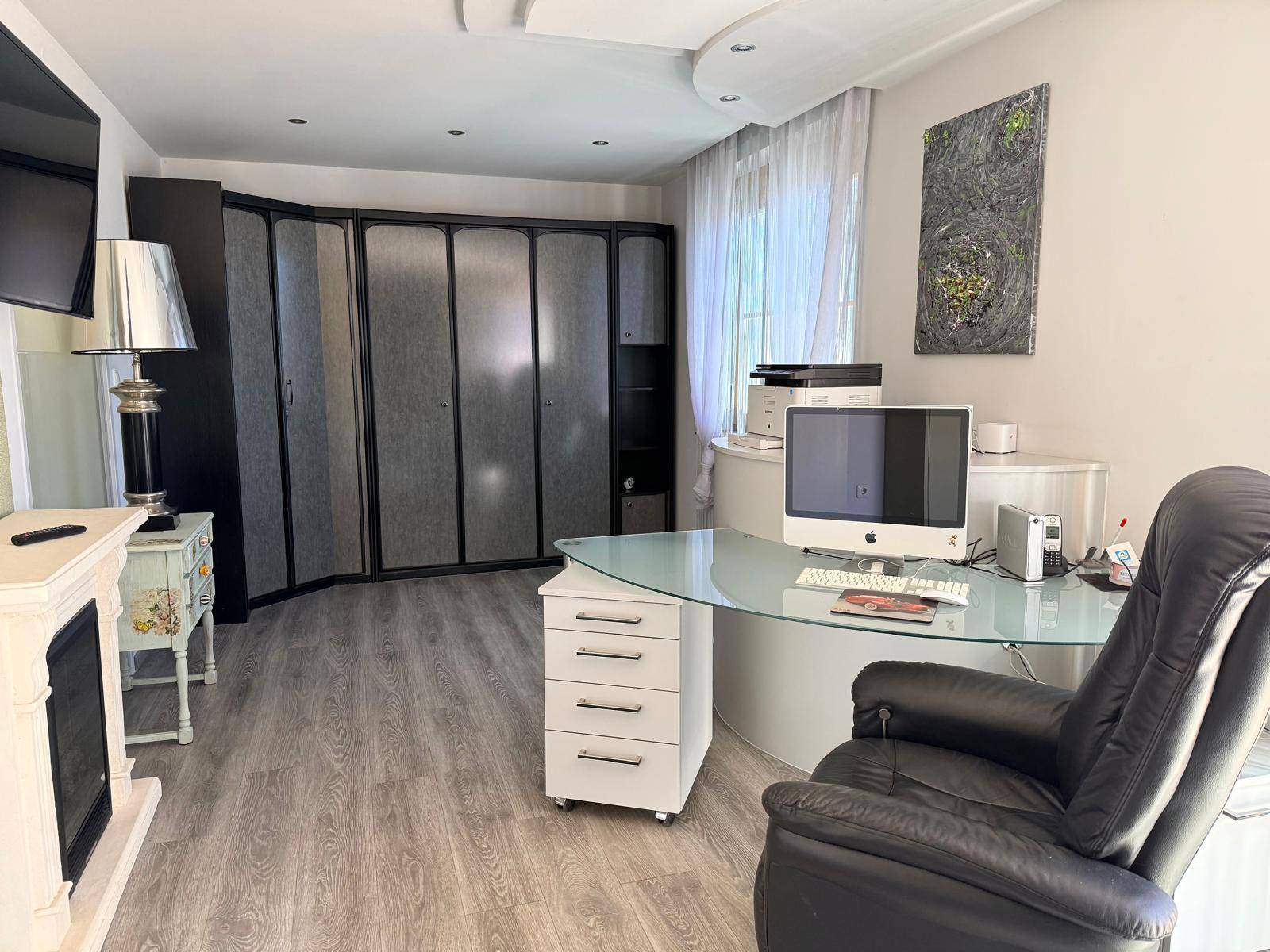 Modernes Büro mit Glas-Schreibtisch, Einbauschränken und großem Fenster für Tageslicht.