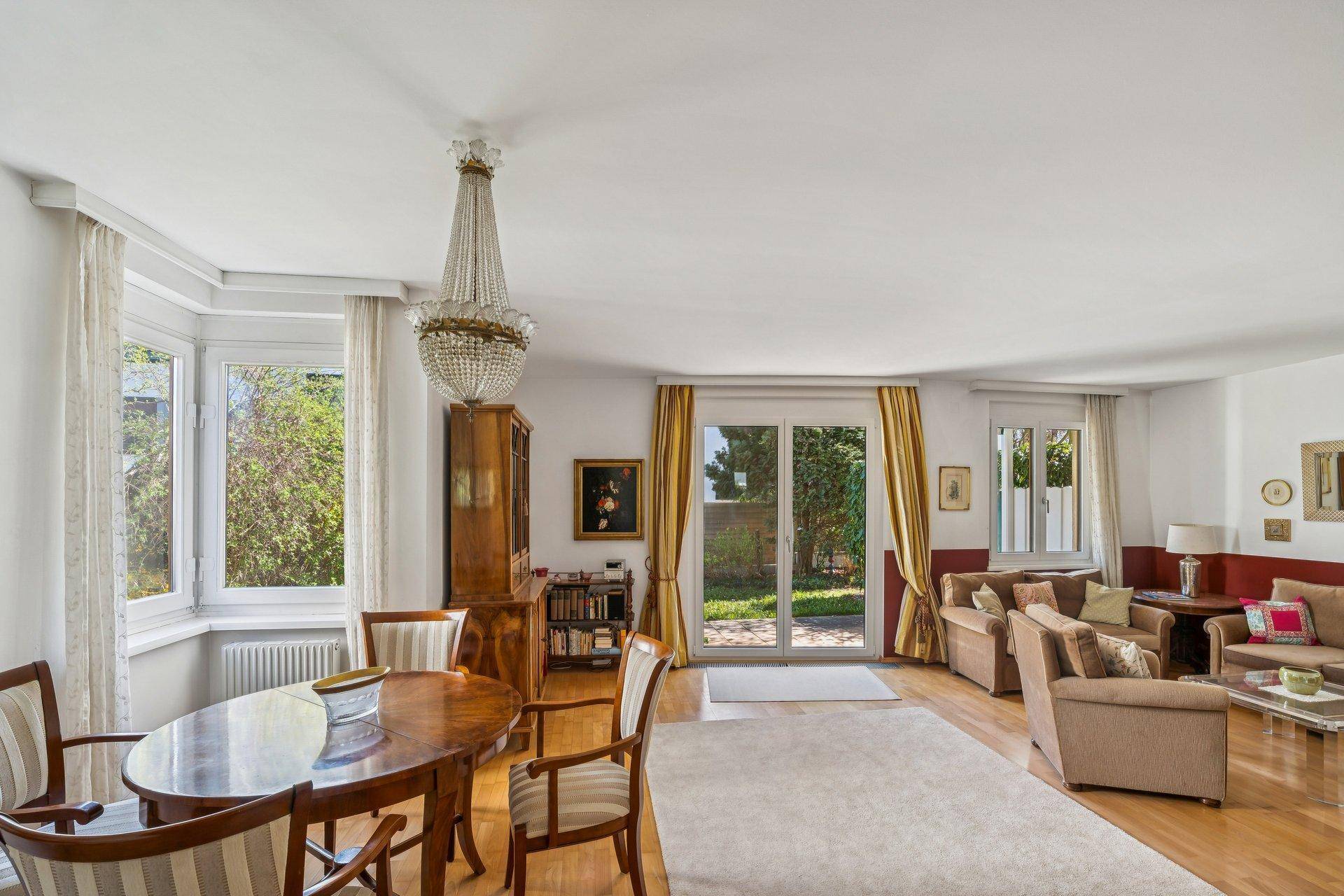 Geräumiger Wohn- und Essbereich mit Parkettboden, Kronleuchter und Zugang zum Garten durch große Fenstertüren.
